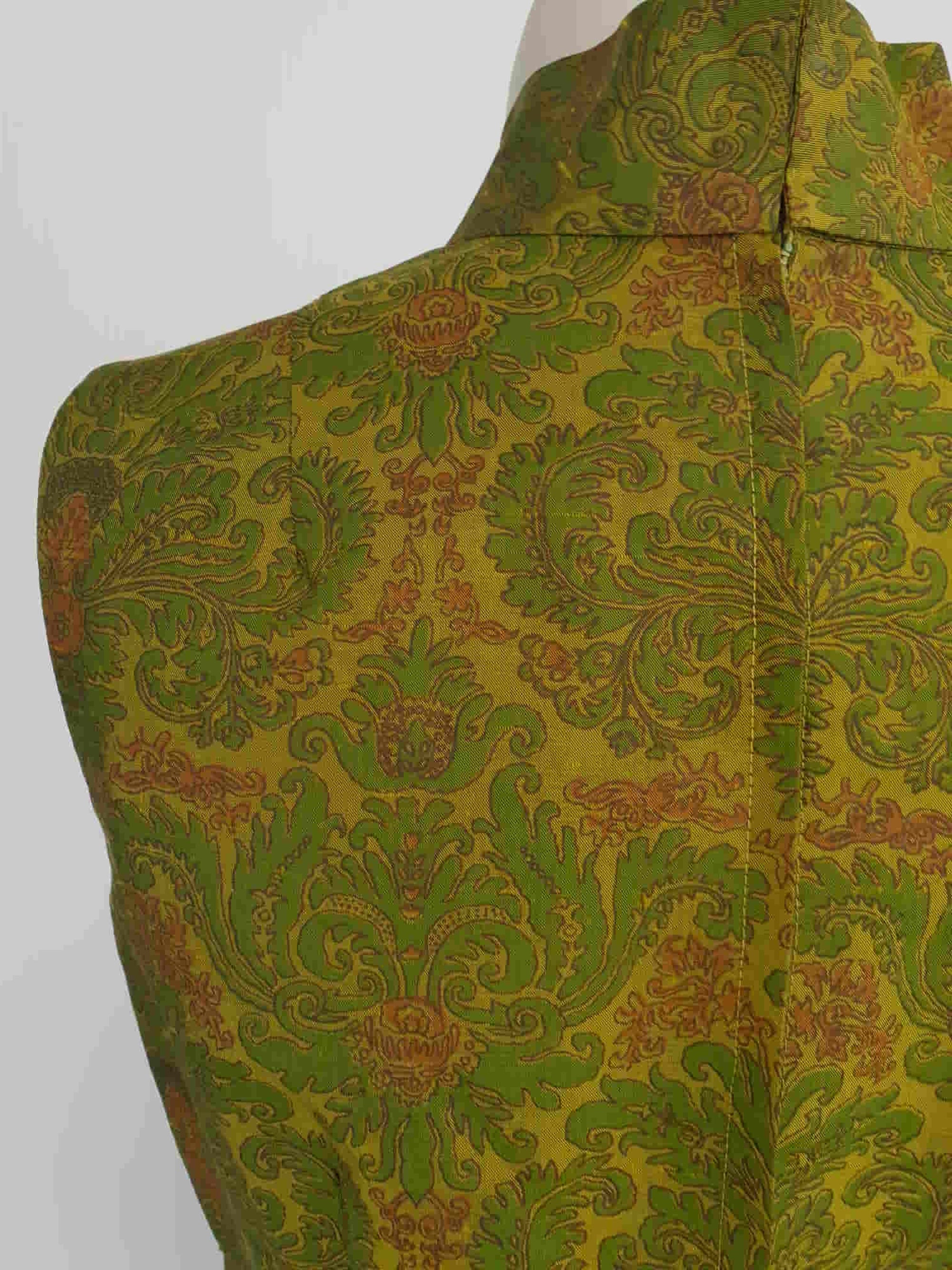 Gorgeous full length formal gown has a stylised Victorian style print in green and coral on a yellow-green ground and overall looks olive green. The fabric is stiff and has a sheen. It has a high standing collar. Closes at the back with a metal zip. The collar closes with hooks and eyes.  Fully lined. Custom made in Hong Kong by Jacky Taylor & Co. Late 1960s - early 1970s. Small.