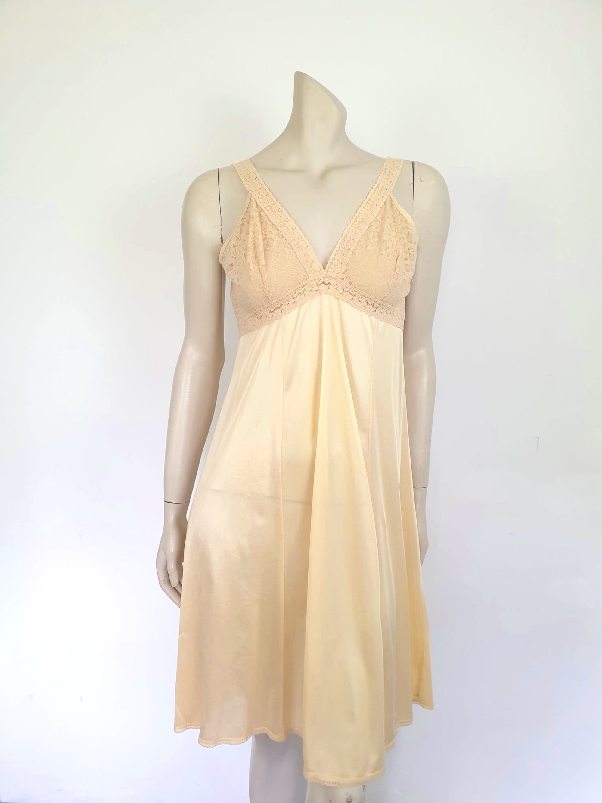 Nude lace slip also works as a nightgown. Below-knee length nude, beige slip has a stretch lace bodice and flared skirt. Wide elastic straps. Narrow lace at the hem. Most of the label is illegible, but I think it says anti-static. Probably nylon. Brand is Rio - 1980s. Medium, Bust 97 cm