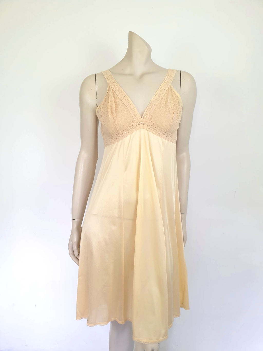 Nude lace slip also works as a nightgown. Below-knee length nude, beige slip has a stretch lace bodice and flared skirt. Wide elastic straps. Narrow lace at the hem. Most of the label is illegible, but I think it says anti-static. Probably nylon. Brand is Rio - 1980s. Medium, Bust 97 cm