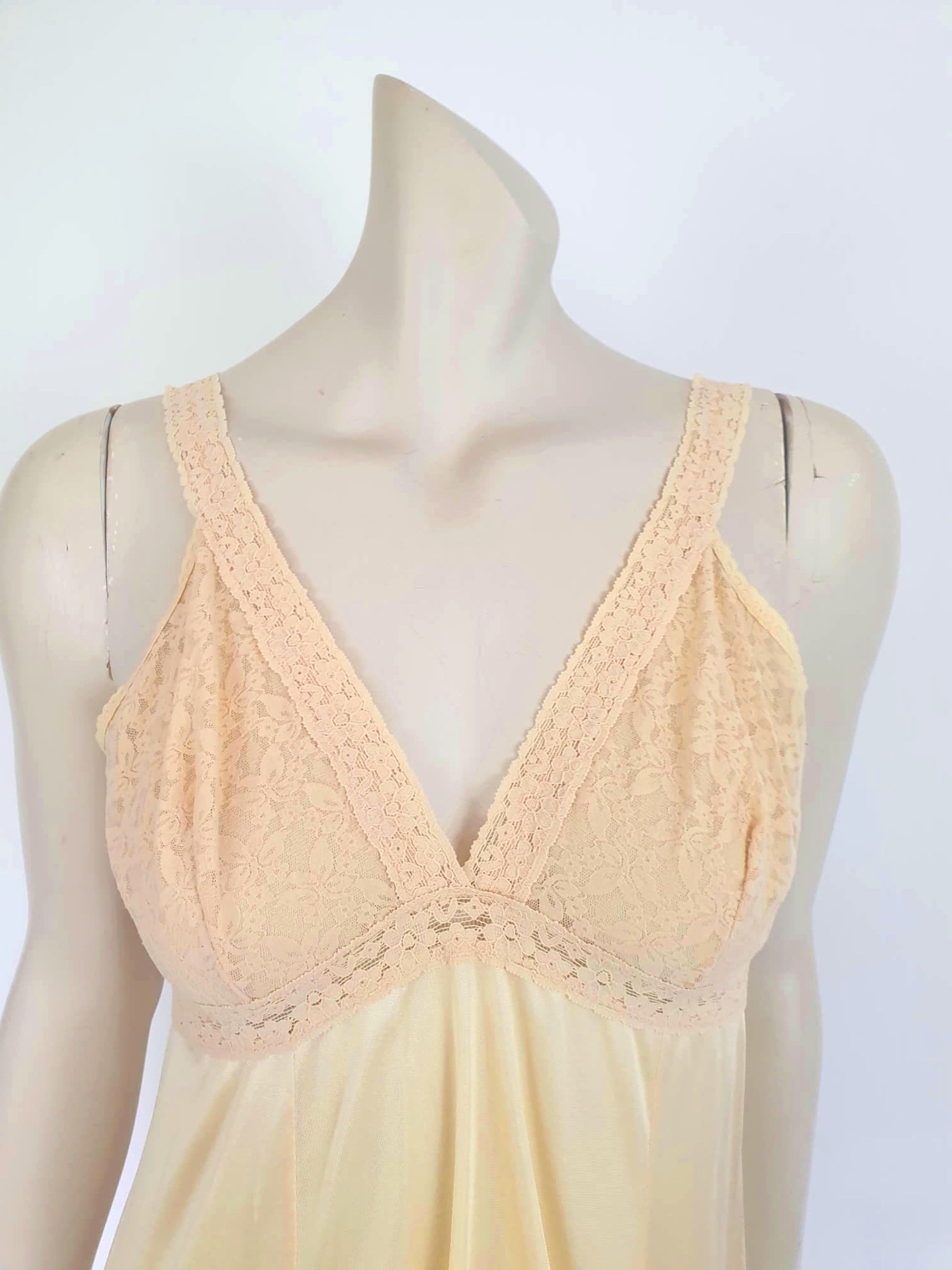 Nude lace slip also works as a nightgown. Below-knee length nude, beige slip has a stretch lace bodice and flared skirt. Wide elastic straps. Narrow lace at the hem. Most of the label is illegible, but I think it says anti-static. Probably nylon. Brand is Rio - 1980s. Medium, Bust 97 cm