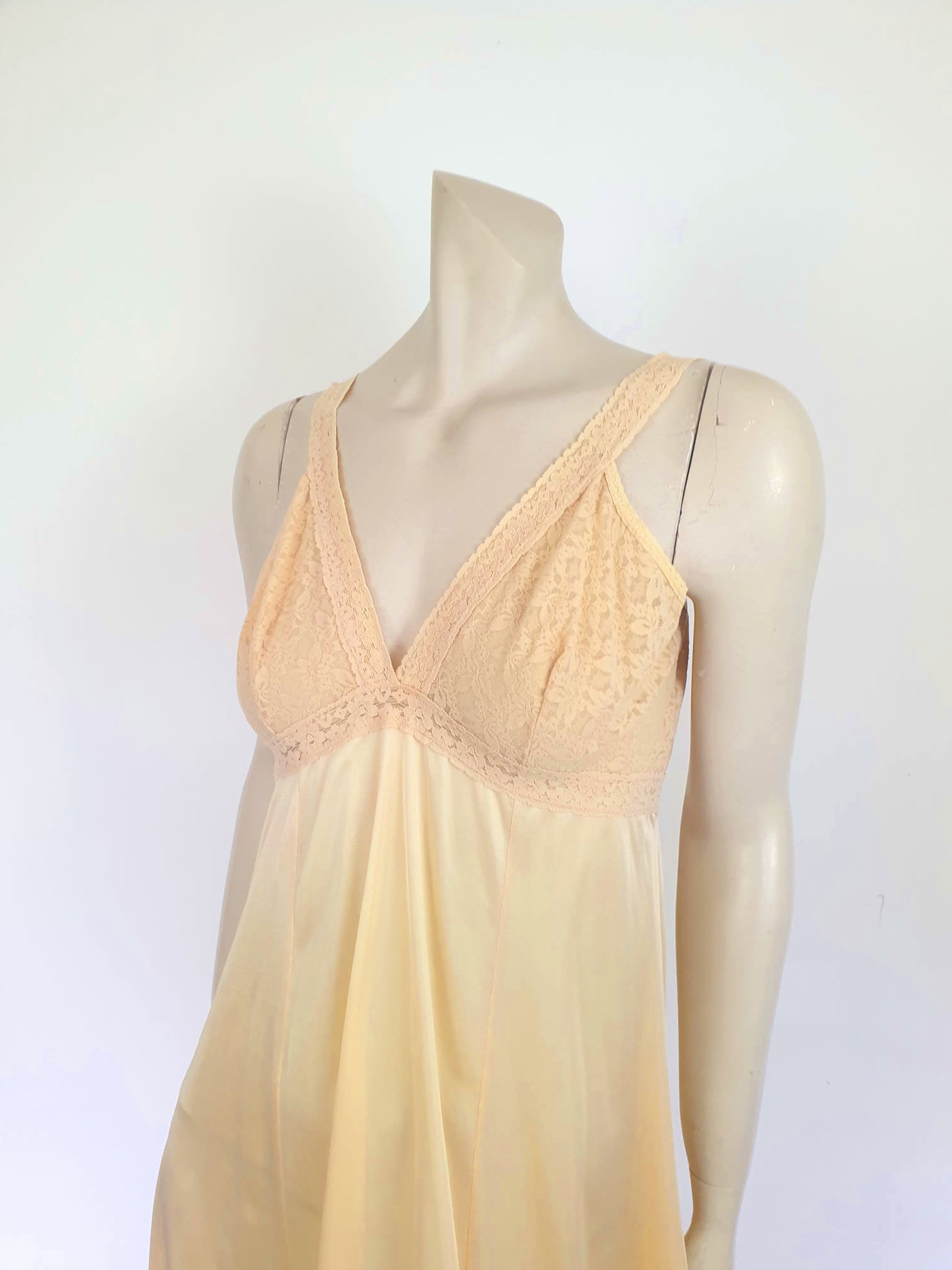 Nude lace slip also works as a nightgown. Below-knee length nude, beige slip has a stretch lace bodice and flared skirt. Wide elastic straps. Narrow lace at the hem. Most of the label is illegible, but I think it says anti-static. Probably nylon. Brand is Rio - 1980s. Medium, Bust 97 cm
