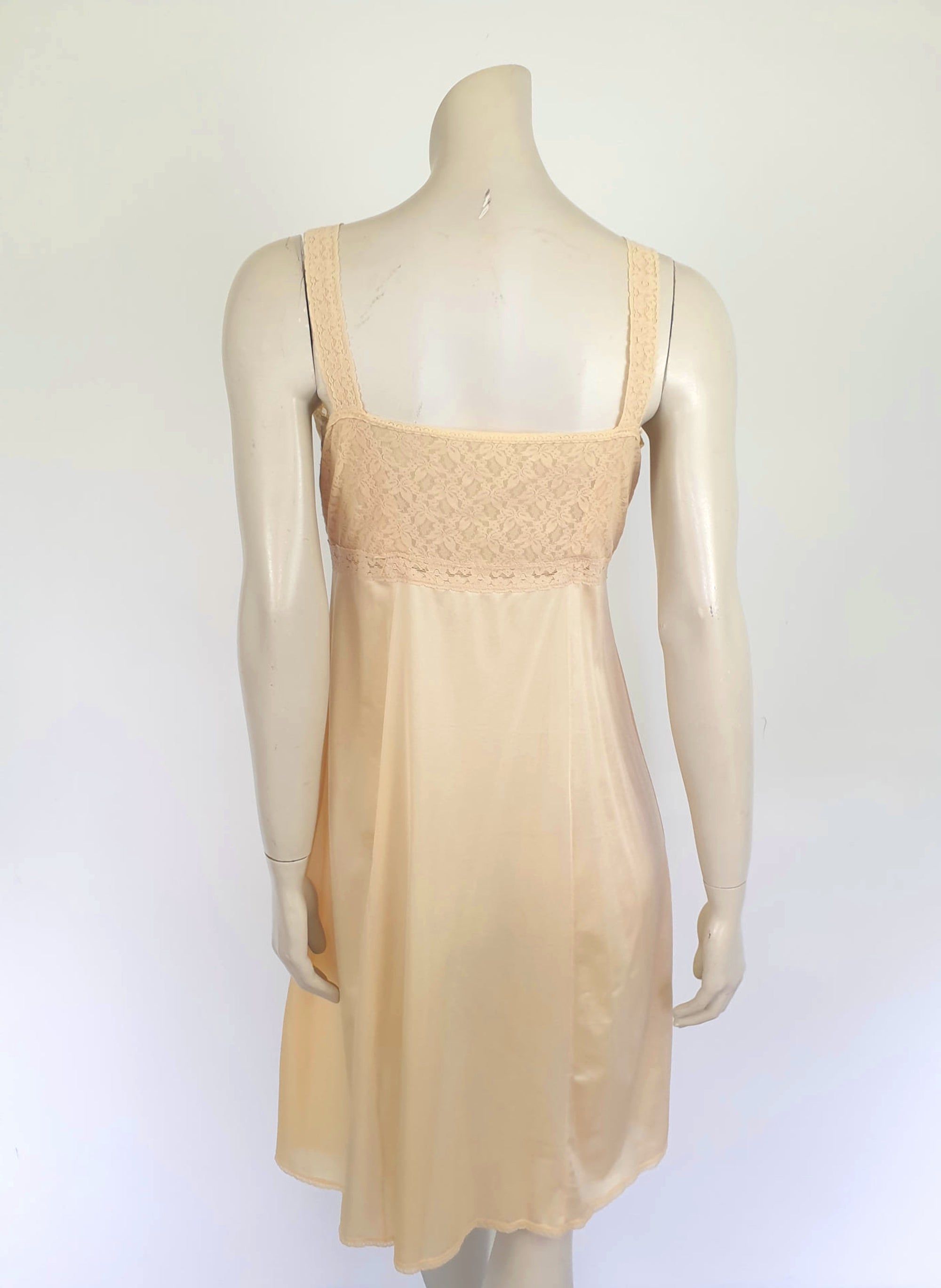 Nude lace slip also works as a nightgown. Below-knee length nude, beige slip has a stretch lace bodice and flared skirt. Wide elastic straps. Narrow lace at the hem. Most of the label is illegible, but I think it says anti-static. Probably nylon. Brand is Rio - 1980s. Medium, Bust 97 cm