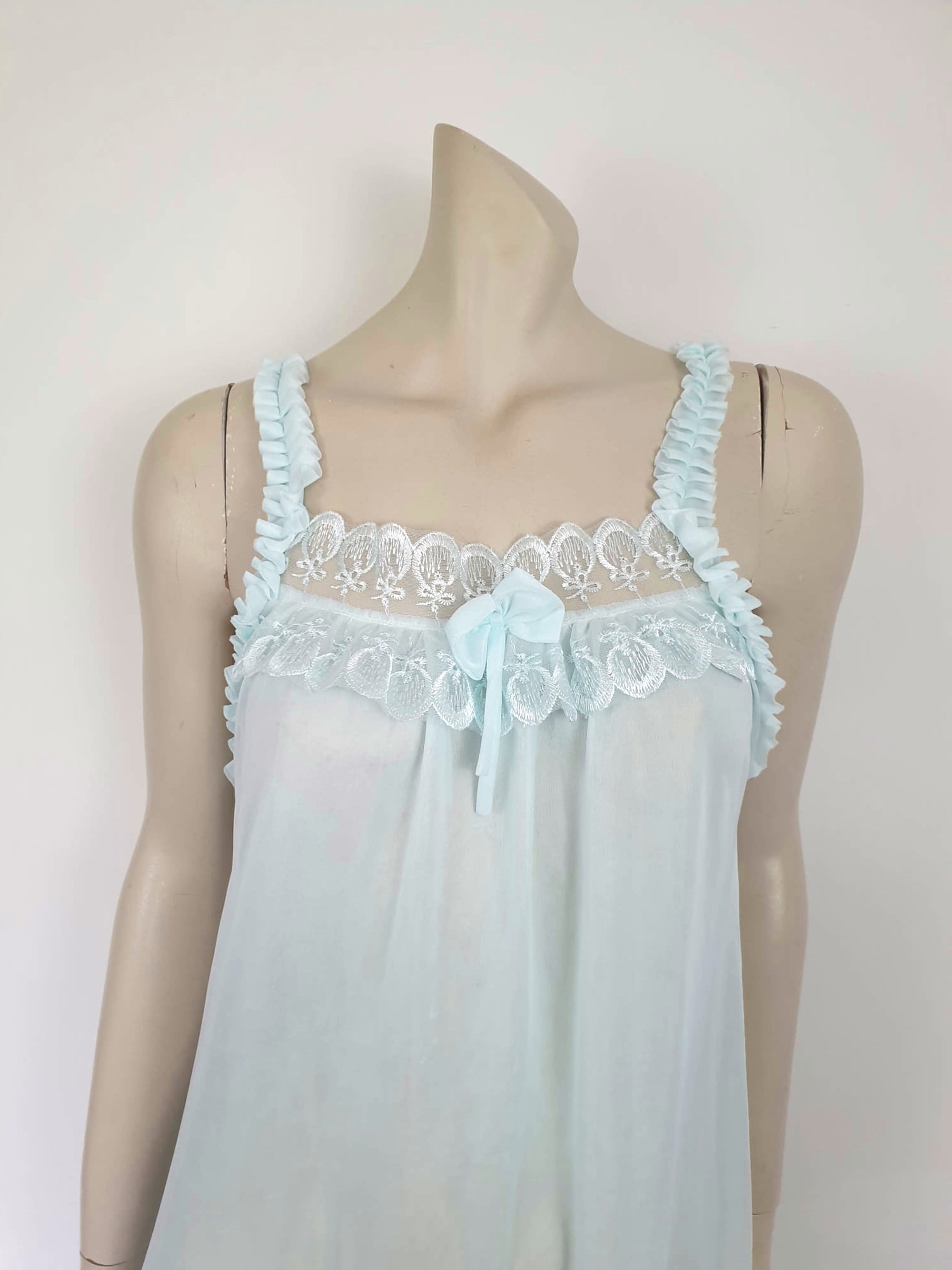 Pretty above knee length blue nightgown has ruffled straps and armholes, lace bodice and front bow. Ruffle at the hemline. Fabric is nylon. No brand label. Made in China. 1980s-1990s.