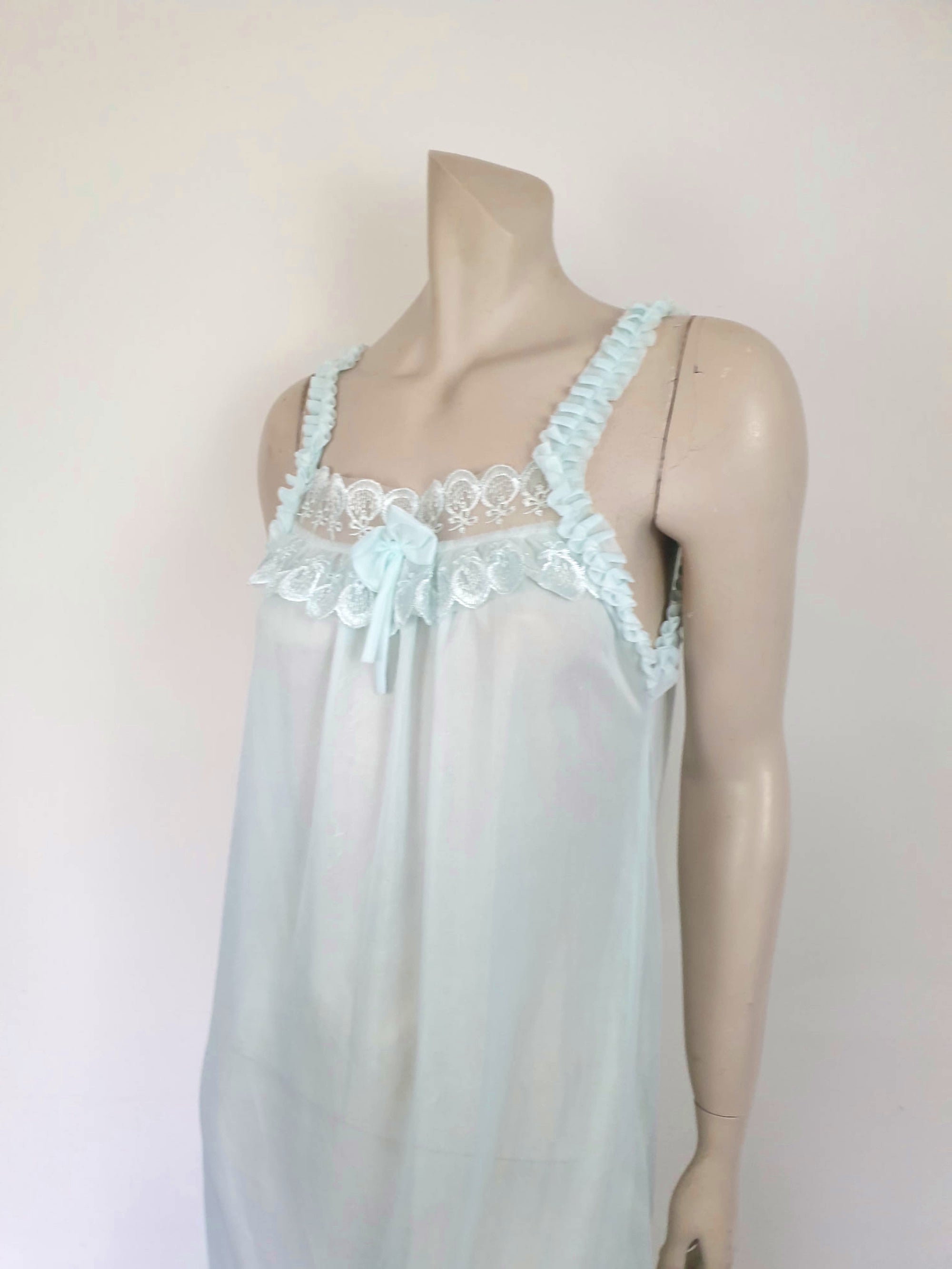 Pretty above knee length blue nightgown has ruffled straps and armholes, lace bodice and front bow. Ruffle at the hemline. Fabric is nylon. No brand label. Made in China. 1980s-1990s.