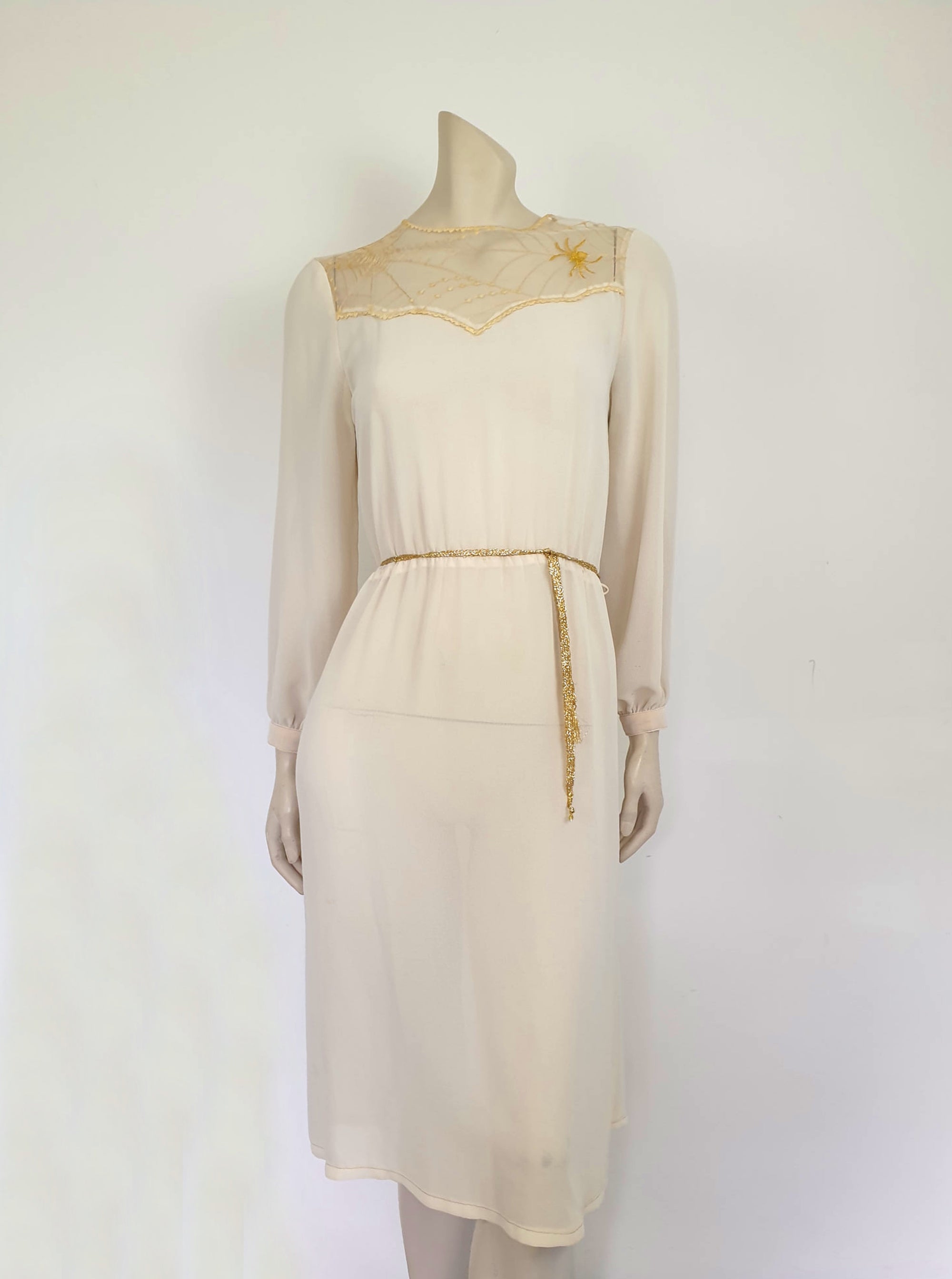 The perfect dress for Halloween, or for those who love spiders and spooky all year round. Pale beige (almost cream) crepe dress with an amazing yoke embroidered with a spiderweb, complete with gold spider. Dress is below-knee length, and has long sleeves which button at the cuffs. It just pulls on over the head and has one button and loop closure at the back neck. There is a separate gold tinsel tie for the waist which runs through carriers. Fabric is polyester. Brand is Ojay - 1970s. Medium.