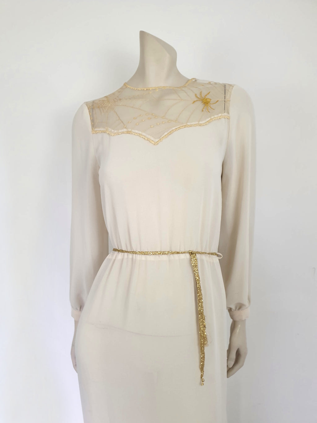 The perfect dress for Halloween, or for those who love spiders and spooky all year round. Pale beige (almost cream) crepe dress with an amazing yoke embroidered with a spiderweb, complete with gold spider. Dress is below-knee length, and has long sleeves which button at the cuffs. It just pulls on over the head and has one button and loop closure at the back neck. There is a separate gold tinsel tie for the waist which runs through carriers. Fabric is polyester. Brand is Ojay - 1970s. Medium.