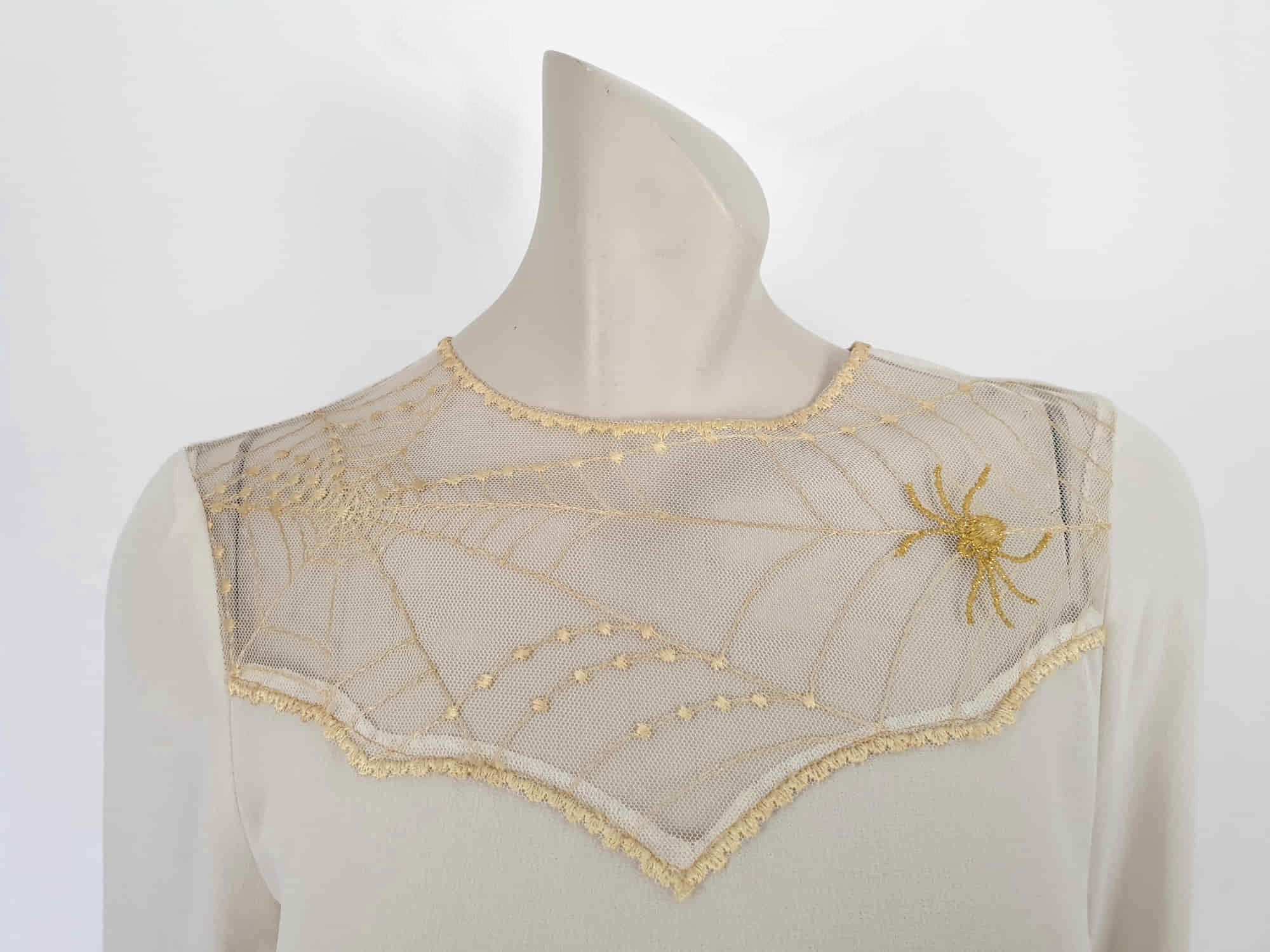 The perfect dress for Halloween, or for those who love spiders and spooky all year round. Pale beige (almost cream) crepe dress with an amazing yoke embroidered with a spiderweb, complete with gold spider. Dress is below-knee length, and has long sleeves which button at the cuffs. It just pulls on over the head and has one button and loop closure at the back neck. There is a separate gold tinsel tie for the waist which runs through carriers. Fabric is polyester. Brand is Ojay - 1970s. Medium.