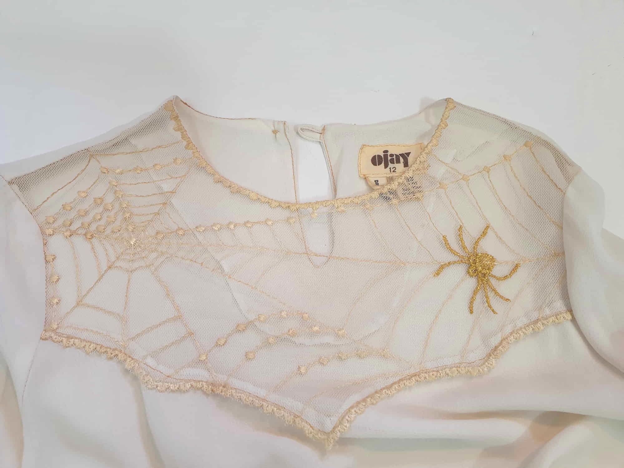 The perfect dress for Halloween, or for those who love spiders and spooky all year round. Pale beige (almost cream) crepe dress with an amazing yoke embroidered with a spiderweb, complete with gold spider. Dress is below-knee length, and has long sleeves which button at the cuffs. It just pulls on over the head and has one button and loop closure at the back neck. There is a separate gold tinsel tie for the waist which runs through carriers. Fabric is polyester. Brand is Ojay - 1970s. Medium.