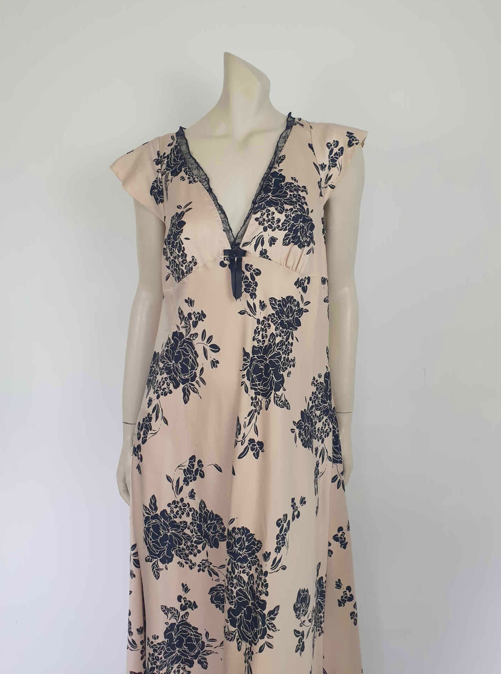 Long beige satin nightgown with large black floral print and flared capped sleeves. The skirt falls from beneath the bust. Slit to the thigh on one side. The V neck is trimmed with narrow black lace and a bow. Elasticised across the back. Fabric is polyester satin. Brand is illegible. 1990s-Y2K?