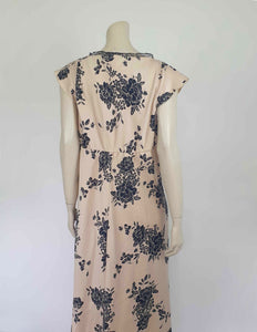 Long beige satin nightgown with large black floral print and flared capped sleeves. The skirt falls from beneath the bust. Slit to the thigh on one side. The V neck is trimmed with narrow black lace and a bow. Elasticised across the back. Fabric is polyester satin. Brand is illegible. 1990s-Y2K?