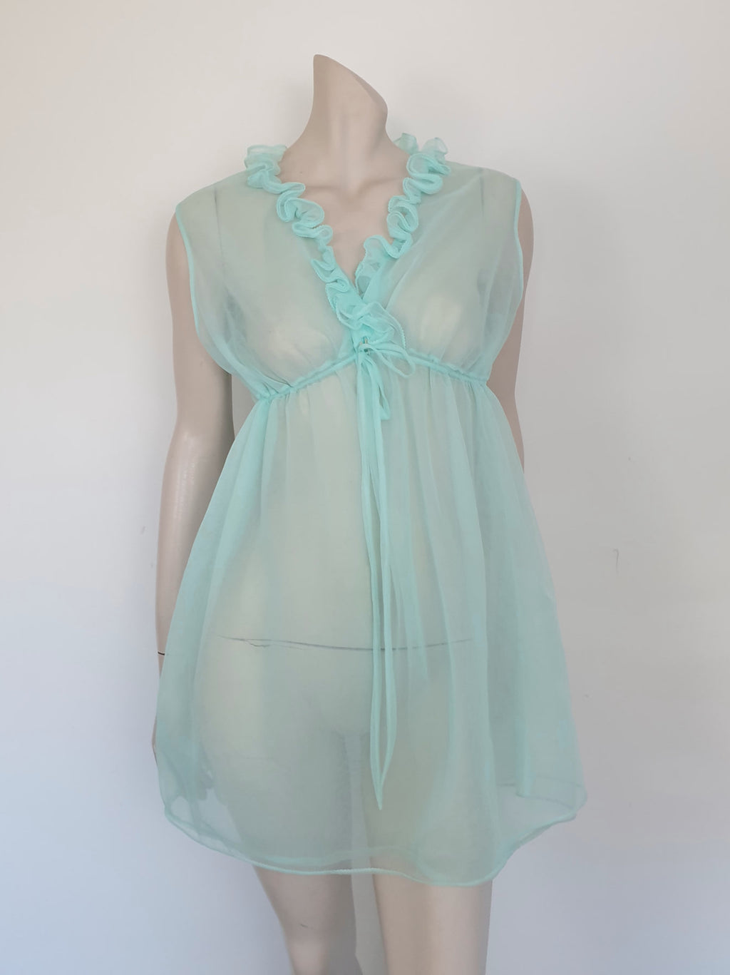 Sheer aqua mini nightgown has a crossover V neck with a drawstring beneath at the front. Double ruffle at the neckline. The back is quite full. Mid-thigh length. It's made from two layers of totally sheer nylon. Brand is Linella - 1960s. Medium.