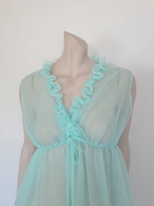 Sheer aqua mini nightgown has a crossover V neck with a drawstring beneath at the front. Double ruffle at the neckline. The back is quite full. Mid-thigh length. It's made from two layers of totally sheer nylon. Brand is Linella - 1960s. Medium.