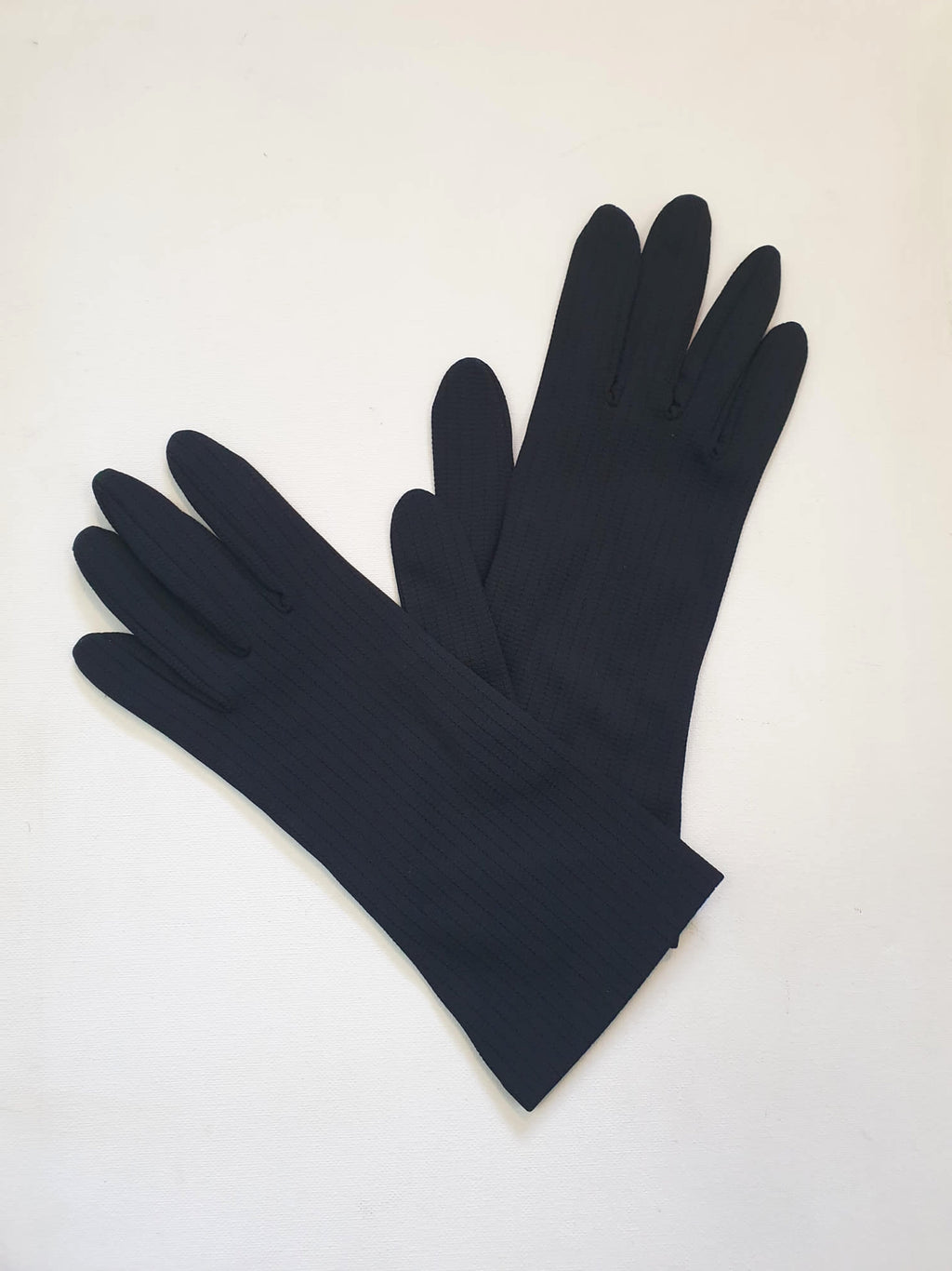 Smart black gloves for a classic dressed up look. Below wrist length stretch gloves have a striped pattern in the weave with a tiny transparent line, giving the look of a line of fine scoring. Mid weight. Fabric is nylon. No brand tag - 1960s. Large.