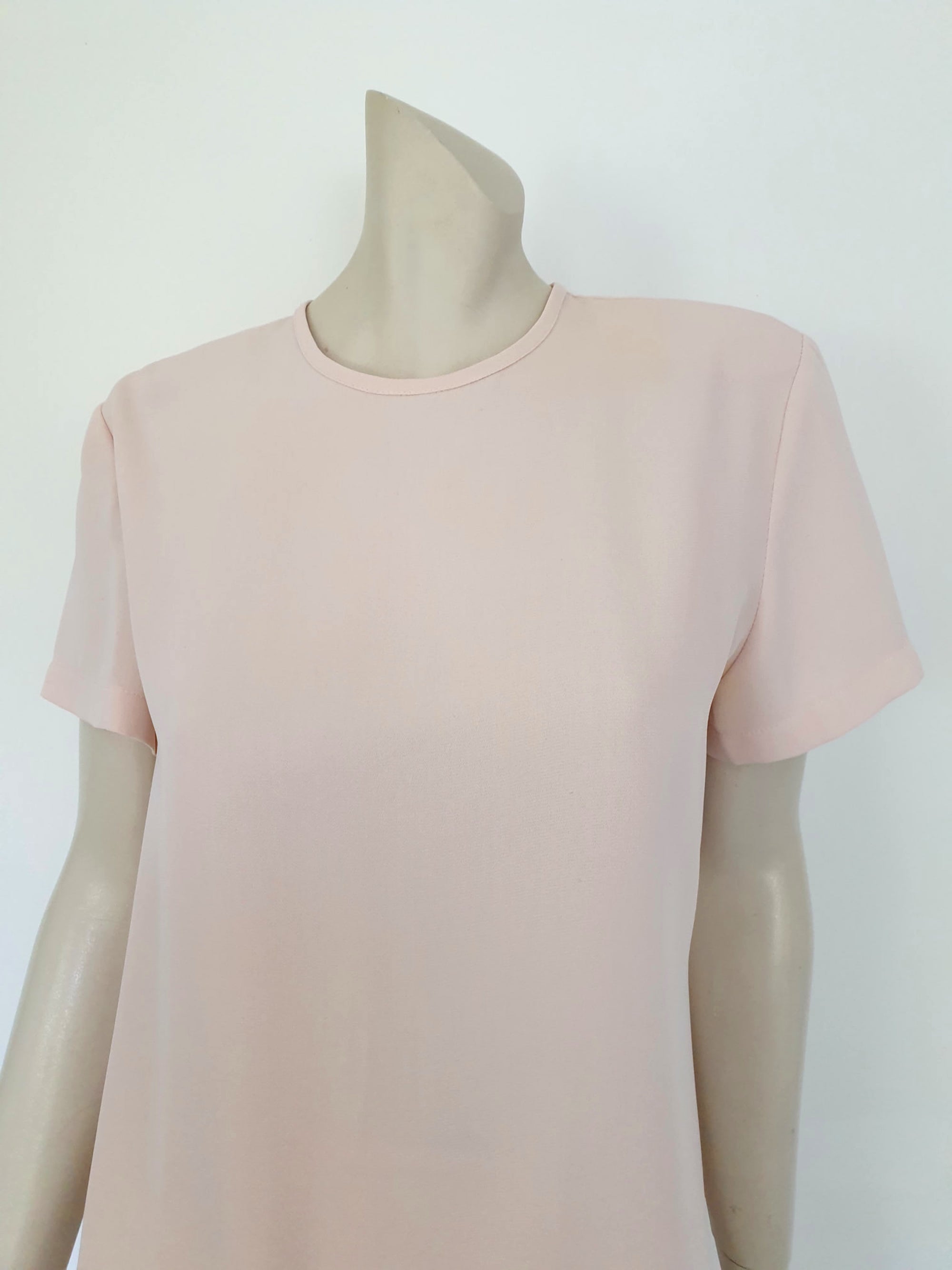 Above-knee length pale pink skirt and top set. Boxy top has short sleeves and is a pullover style, with a short opening buttoning at the back of the neck. There are removable shoulder pads. The straight skirt has a rear vent, rear zip and button fastening and is lined. Fabric is polyester crepe. Made in New Zealand for Suzanne Gregory - 1980s. Medium to Large.