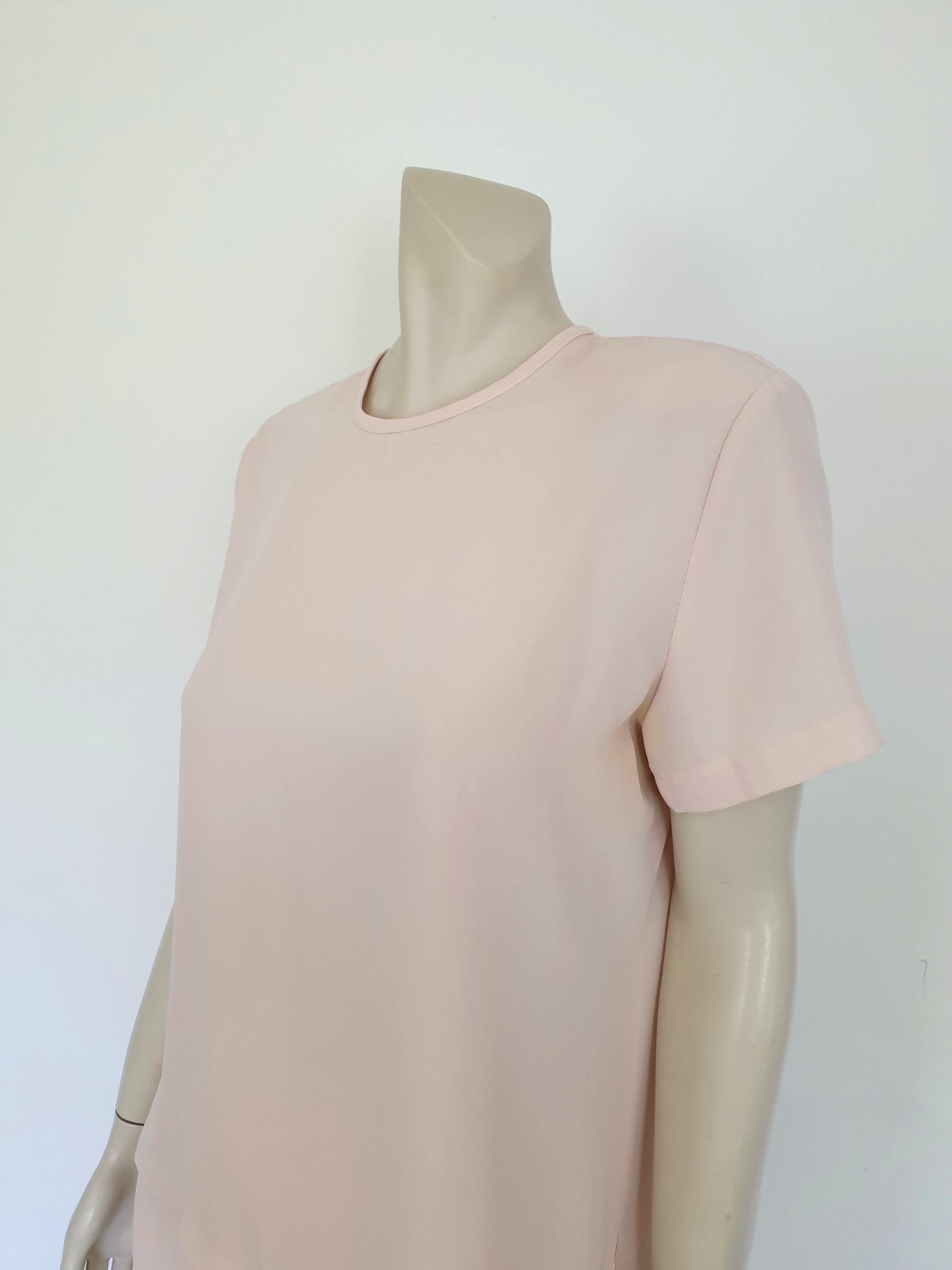 Above-knee length pale pink skirt and top set. Boxy top has short sleeves and is a pullover style, with a short opening buttoning at the back of the neck. There are removable shoulder pads. The straight skirt has a rear vent, rear zip and button fastening and is lined. Fabric is polyester crepe. Made in New Zealand for Suzanne Gregory - 1980s. Medium to Large.