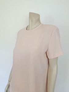 Above-knee length pale pink skirt and top set. Boxy top has short sleeves and is a pullover style, with a short opening buttoning at the back of the neck. There are removable shoulder pads. The straight skirt has a rear vent, rear zip and button fastening and is lined. Fabric is polyester crepe. Made in New Zealand for Suzanne Gregory - 1980s. Medium to Large.