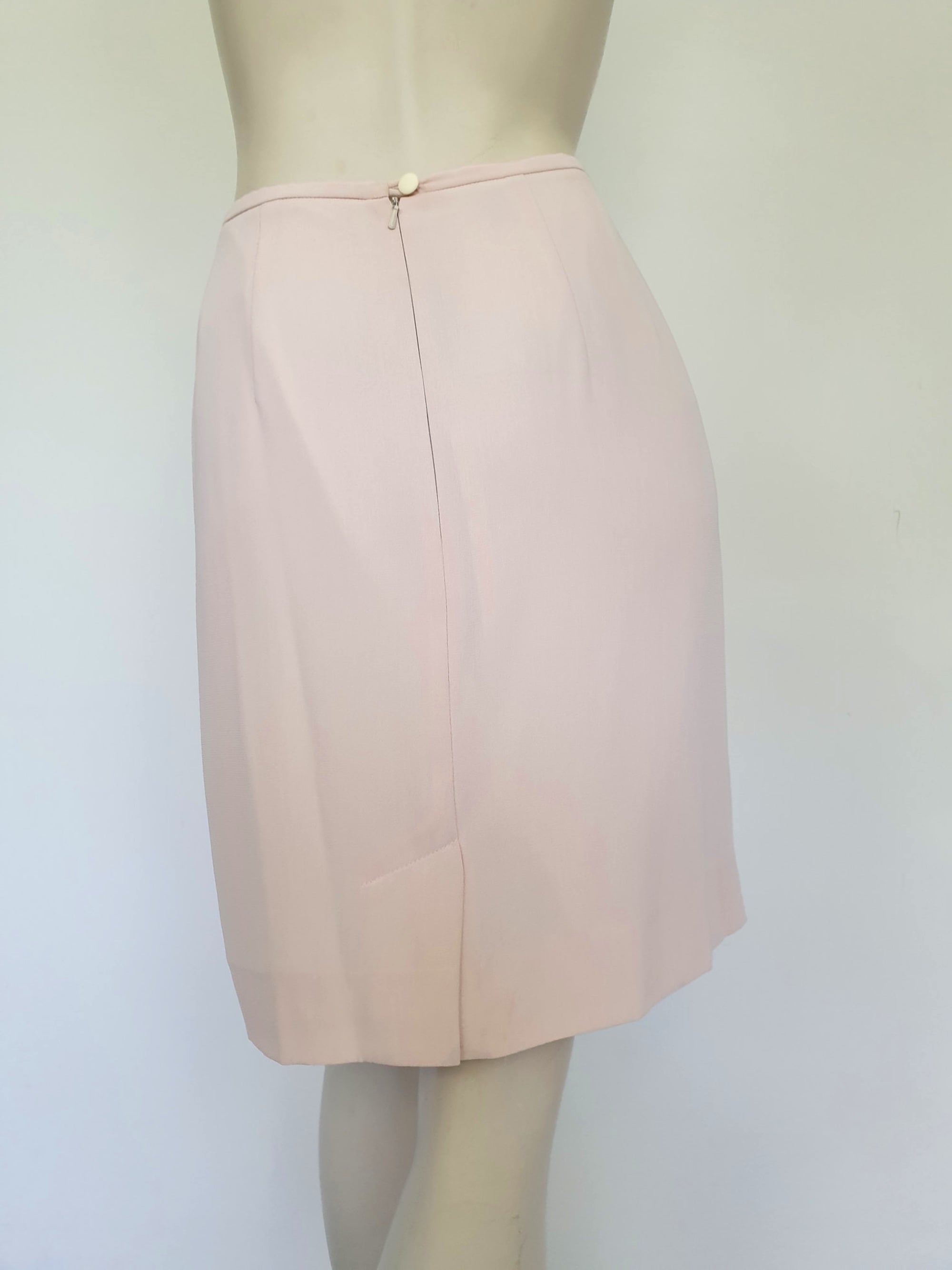 Above-knee length pale pink skirt and top set. Boxy top has short sleeves and is a pullover style, with a short opening buttoning at the back of the neck. There are removable shoulder pads. The straight skirt has a rear vent, rear zip and button fastening and is lined. Fabric is polyester crepe. Made in New Zealand for Suzanne Gregory - 1980s. Medium to Large.