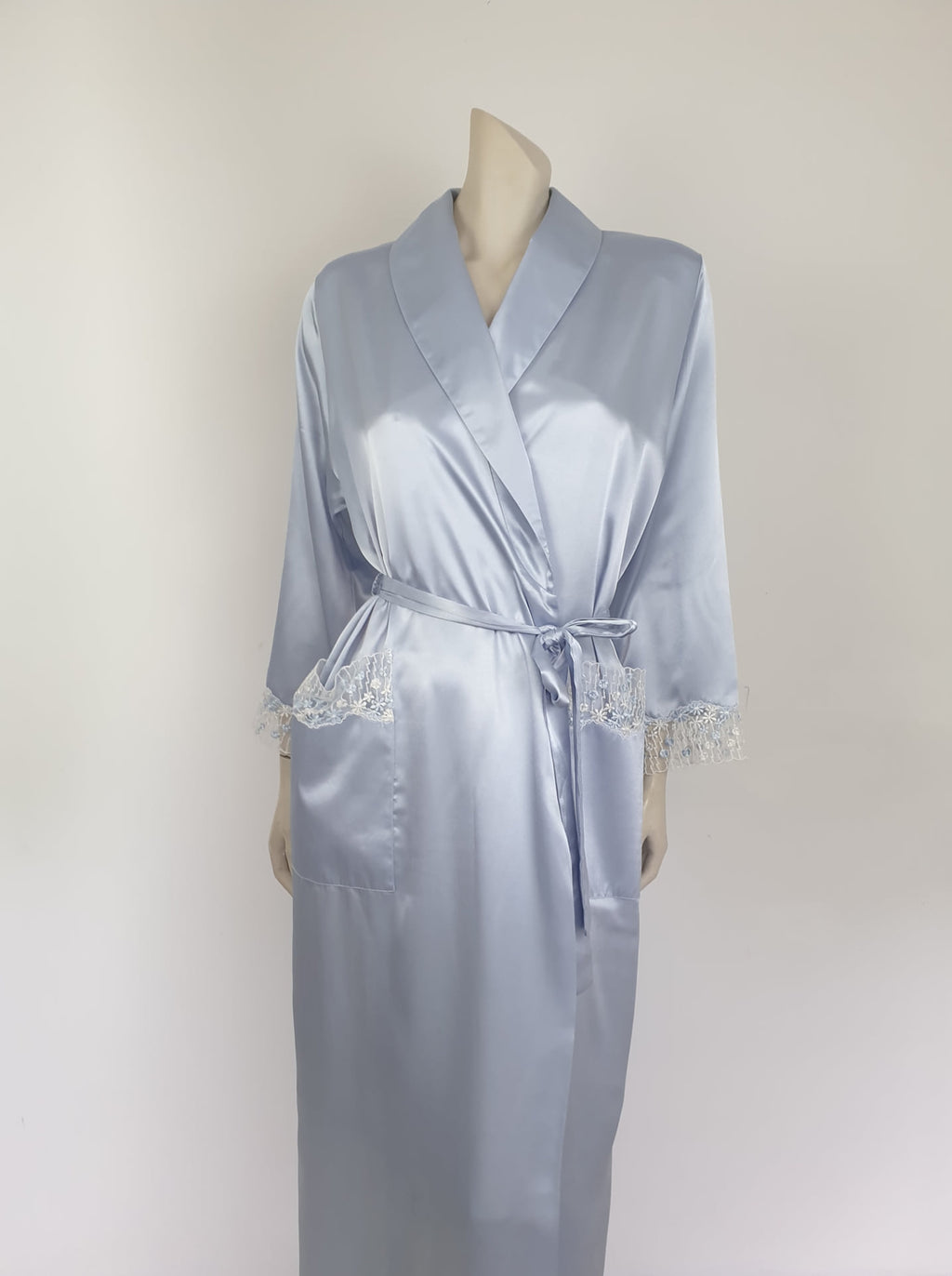 Beautiful blue satin robe with two patch pockets. Sleeves and pockets are trimmed with wide blue and white lace. Shawl collar and separate tie through carriers at the waist. Shoulder pads. Fabric is polyester satin. Made under licence in Australia for a famous French designer, see label - 1980s.