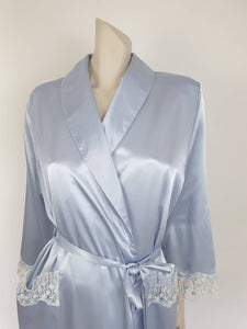 Beautiful blue satin robe with two patch pockets. Sleeves and pockets are trimmed with wide blue and white lace. Shawl collar and separate tie through carriers at the waist. Shoulder pads. Fabric is polyester satin. Made under licence in Australia for a famous French designer, see label - 1980s.
