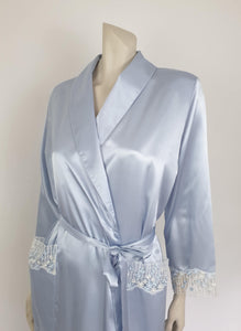 Beautiful blue satin robe with two patch pockets. Sleeves and pockets are trimmed with wide blue and white lace. Shawl collar and separate tie through carriers at the waist. Shoulder pads. Fabric is polyester satin. Made under licence in Australia for a famous French designer, see label - 1980s.