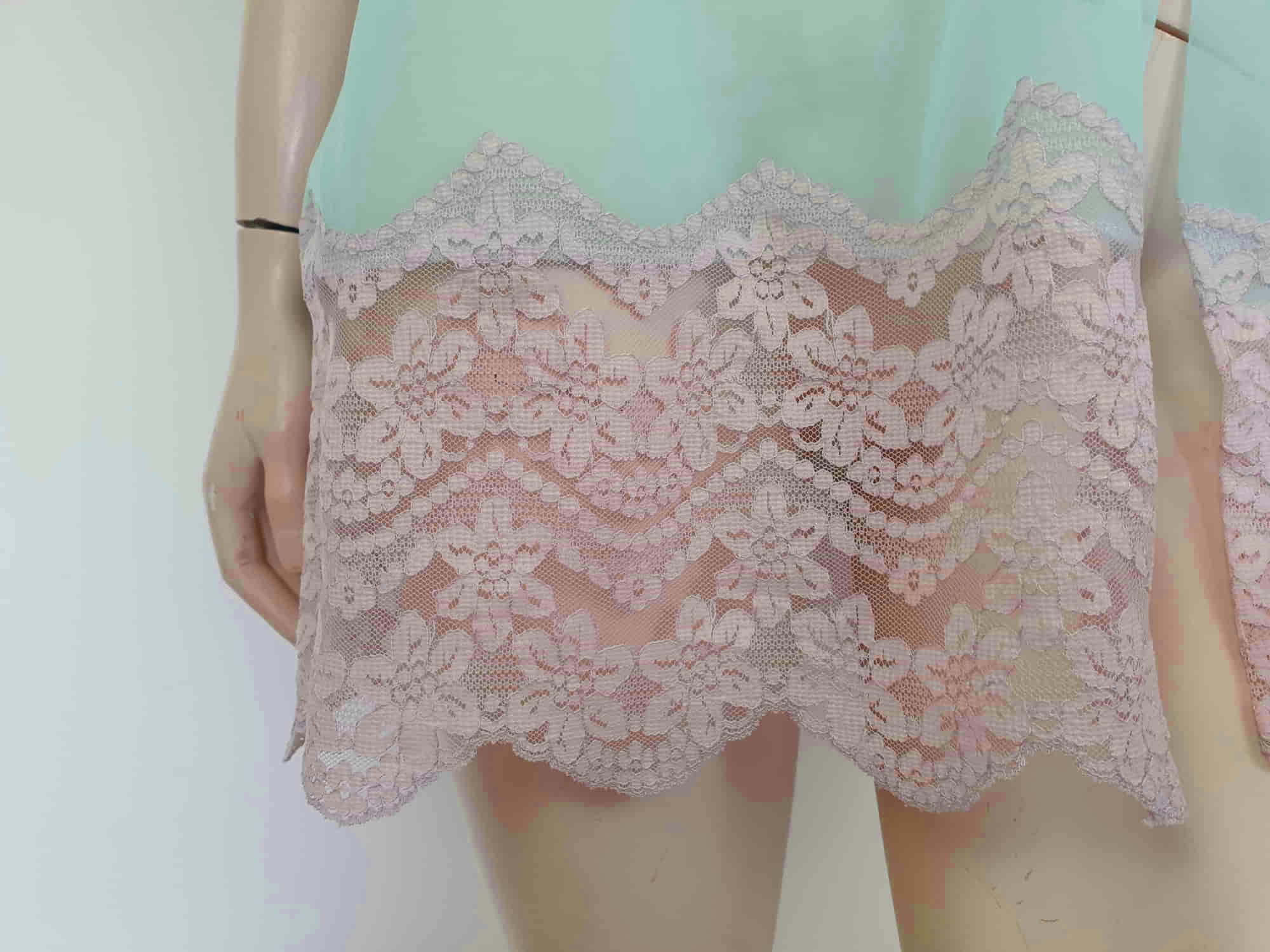 Thigh length robe has a V-neckline and wide pinky-beige lace at the below-elbow length sleeves and hem. Small bow at the neck. Closes at the front with one press stud.  The fabric is a double layer of sheer nylon. Made in the USA for Gilead - 1960s. Medium