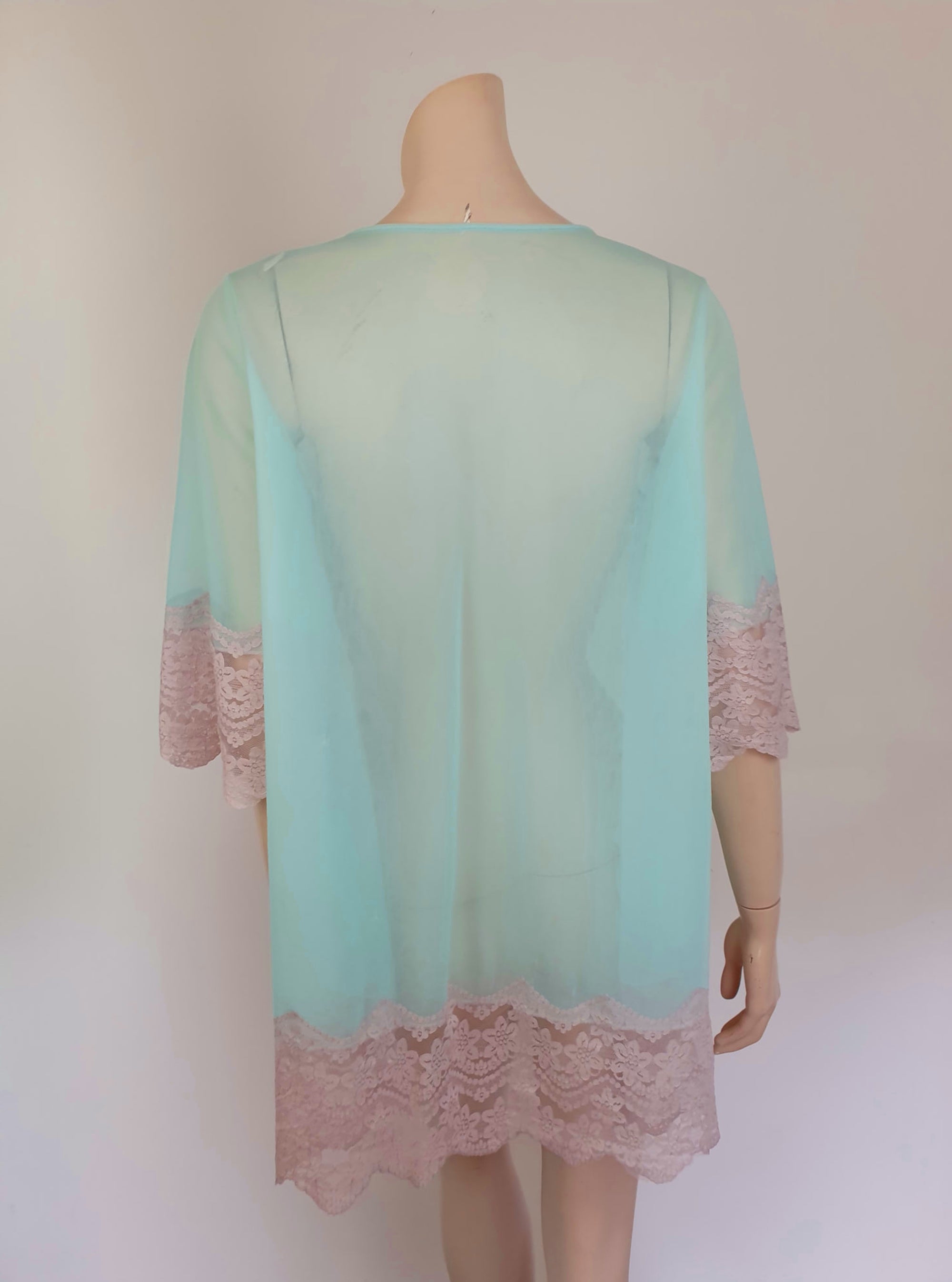 Thigh length robe has a V-neckline and wide pinky-beige lace at the below-elbow length sleeves and hem. Small bow at the neck. Closes at the front with one press stud.  The fabric is a double layer of sheer nylon. Made in the USA for Gilead - 1960s. Medium