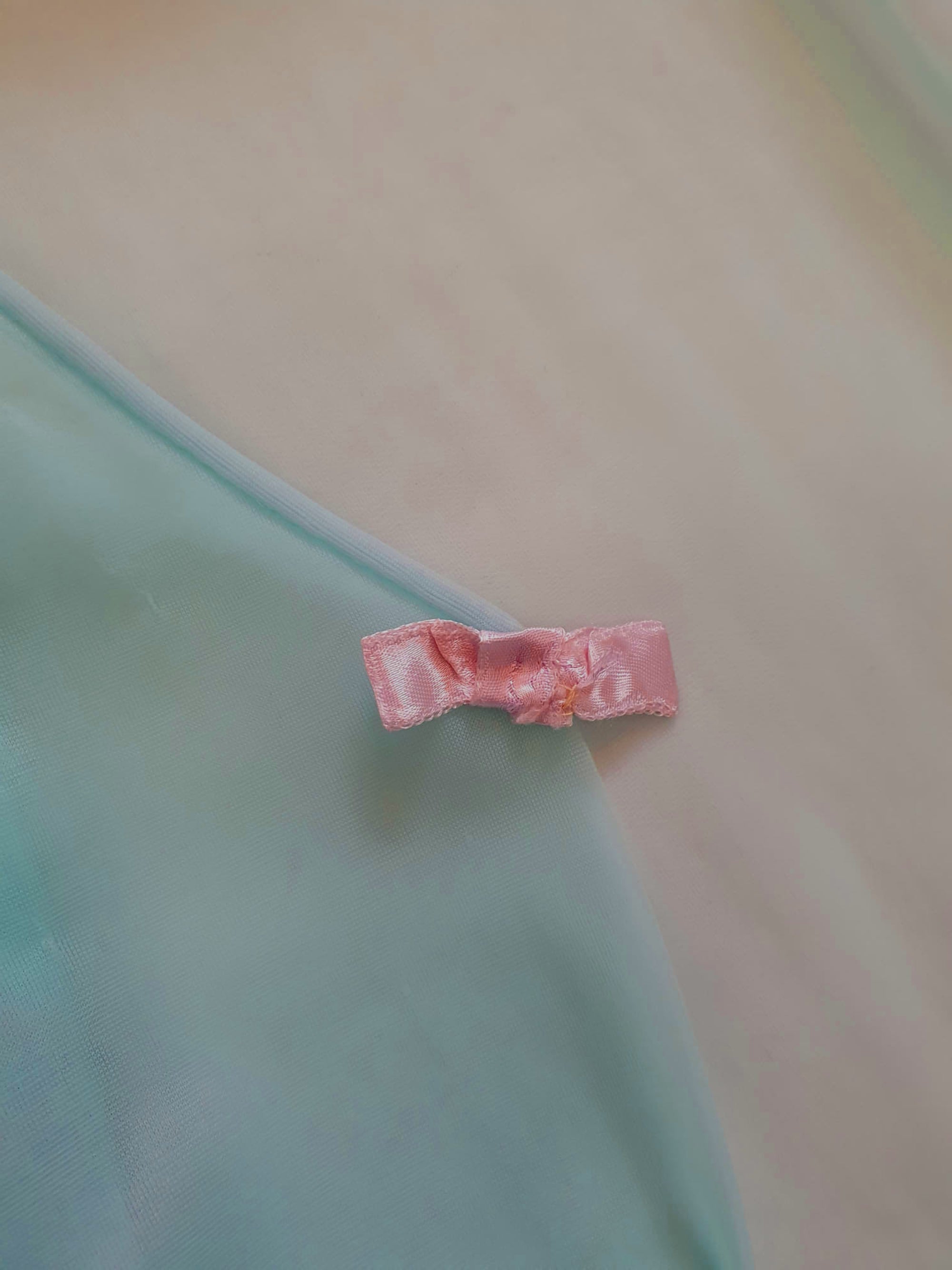 Thigh length robe has a V-neckline and wide pinky-beige lace at the below-elbow length sleeves and hem. Small bow at the neck. Closes at the front with one press stud.  The fabric is a double layer of sheer nylon. Made in the USA for Gilead - 1960s. Medium