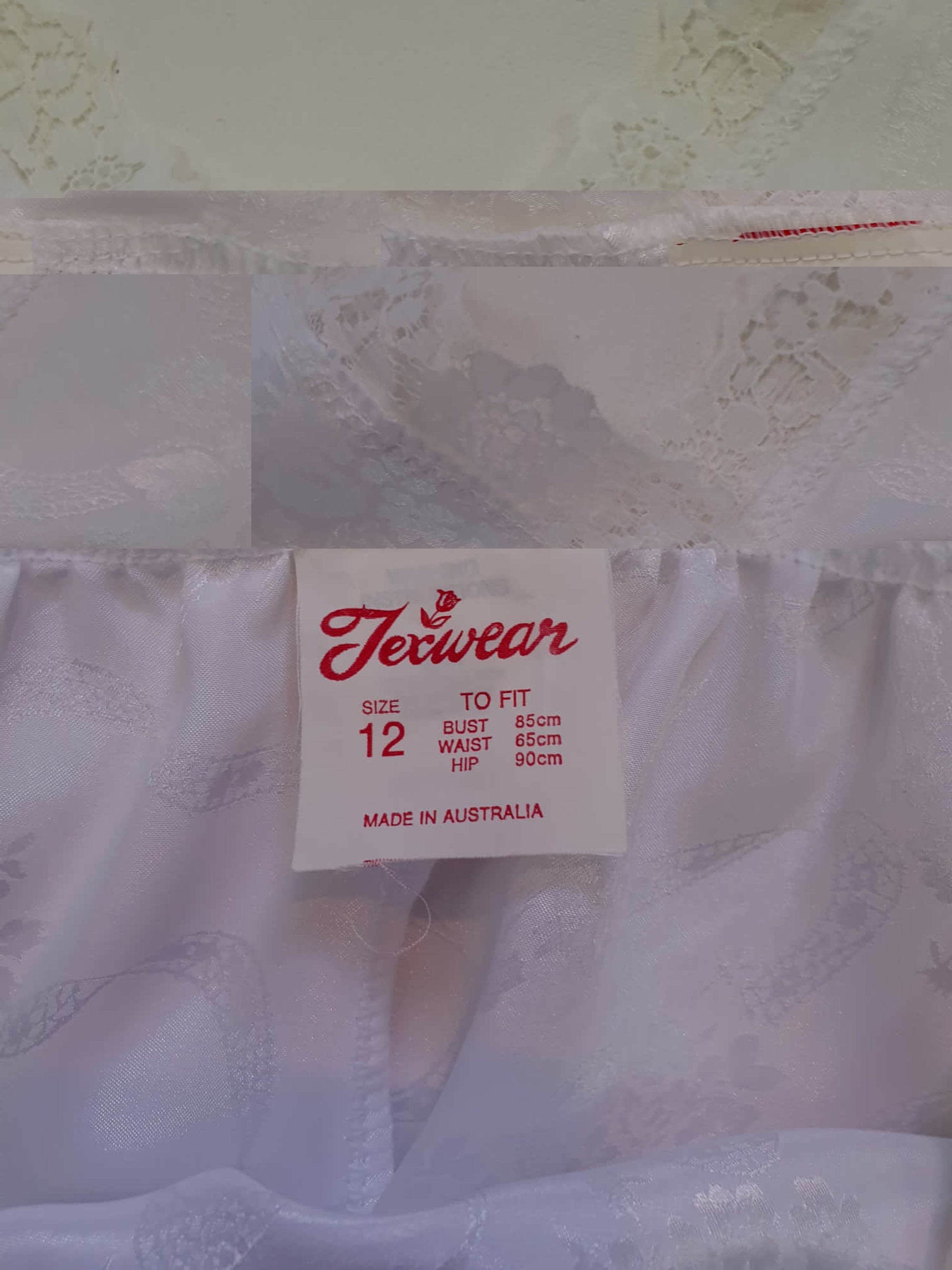 White satin nightgown has a lacy yoke, V-neck and has lace trim at the neckline, armholes and hem. The beautiful fabric is a damask weave with a floral design. Closes at the neck with one button and a ribbon bow. The nightie is mid to lower calf length. Fabric is polyester. Made in Australia by Texwear - 1980s. Medium