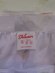 White satin nightgown has a lacy yoke, V-neck and has lace trim at the neckline, armholes and hem. The beautiful fabric is a damask weave with a floral design. Closes at the neck with one button and a ribbon bow. The nightie is mid to lower calf length. Fabric is polyester. Made in Australia by Texwear - 1980s. Medium