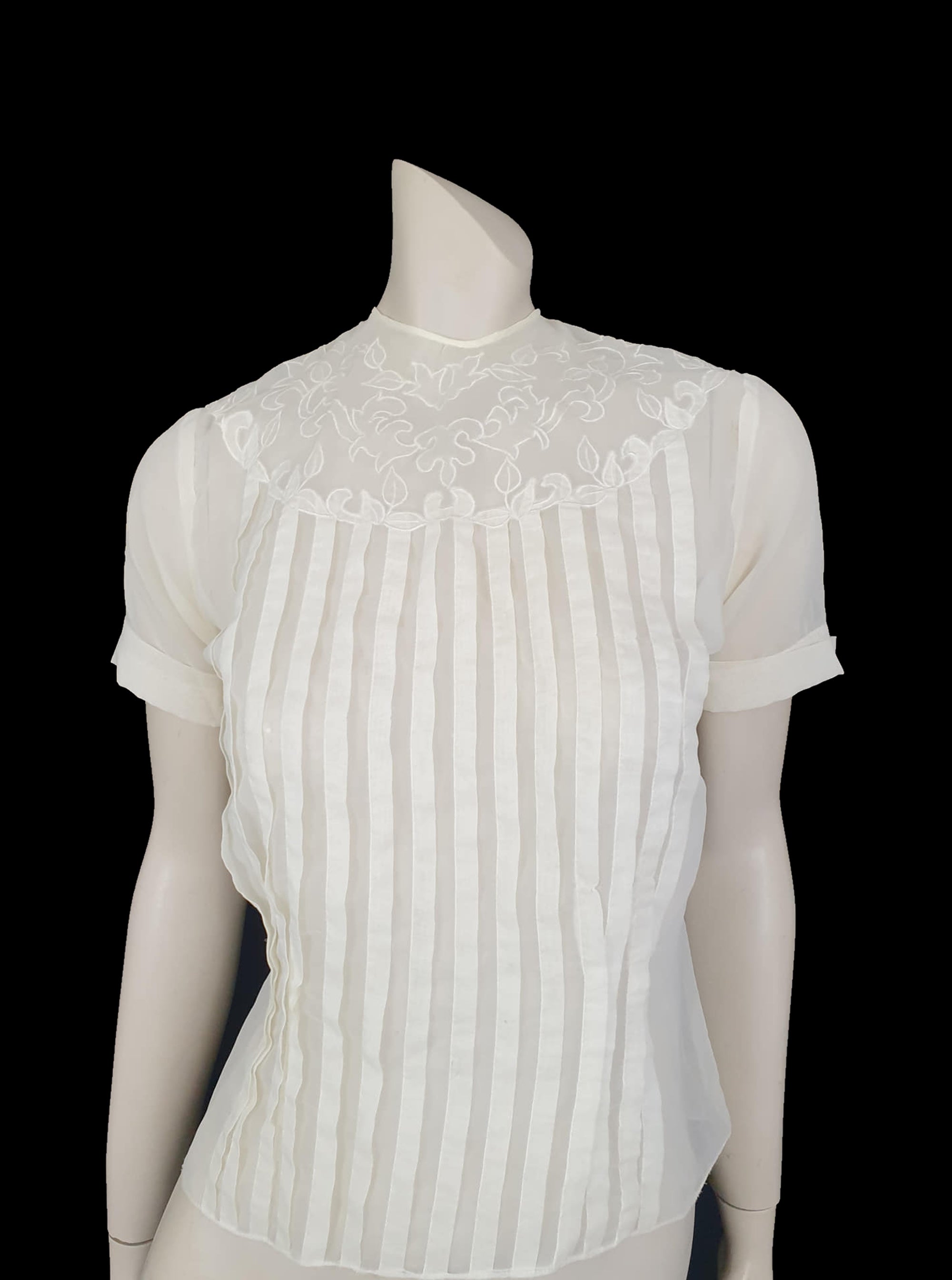 Beautiful little button back blouse - so pretty and feminine. Totally sheer nylon blouse has vertical tucks across the front and a circular yoke embellished with dainty applique work. The short sleeves have turn back cuffs. You will need to have someone to help you get dressed as it buttons down the back with shell buttons. It's darted in at the waist as it was designed to be tucked into a very high-waisted skirt. Brand is Park Lane, late 1950s-early 1960s. fits bust 92 cm/36".