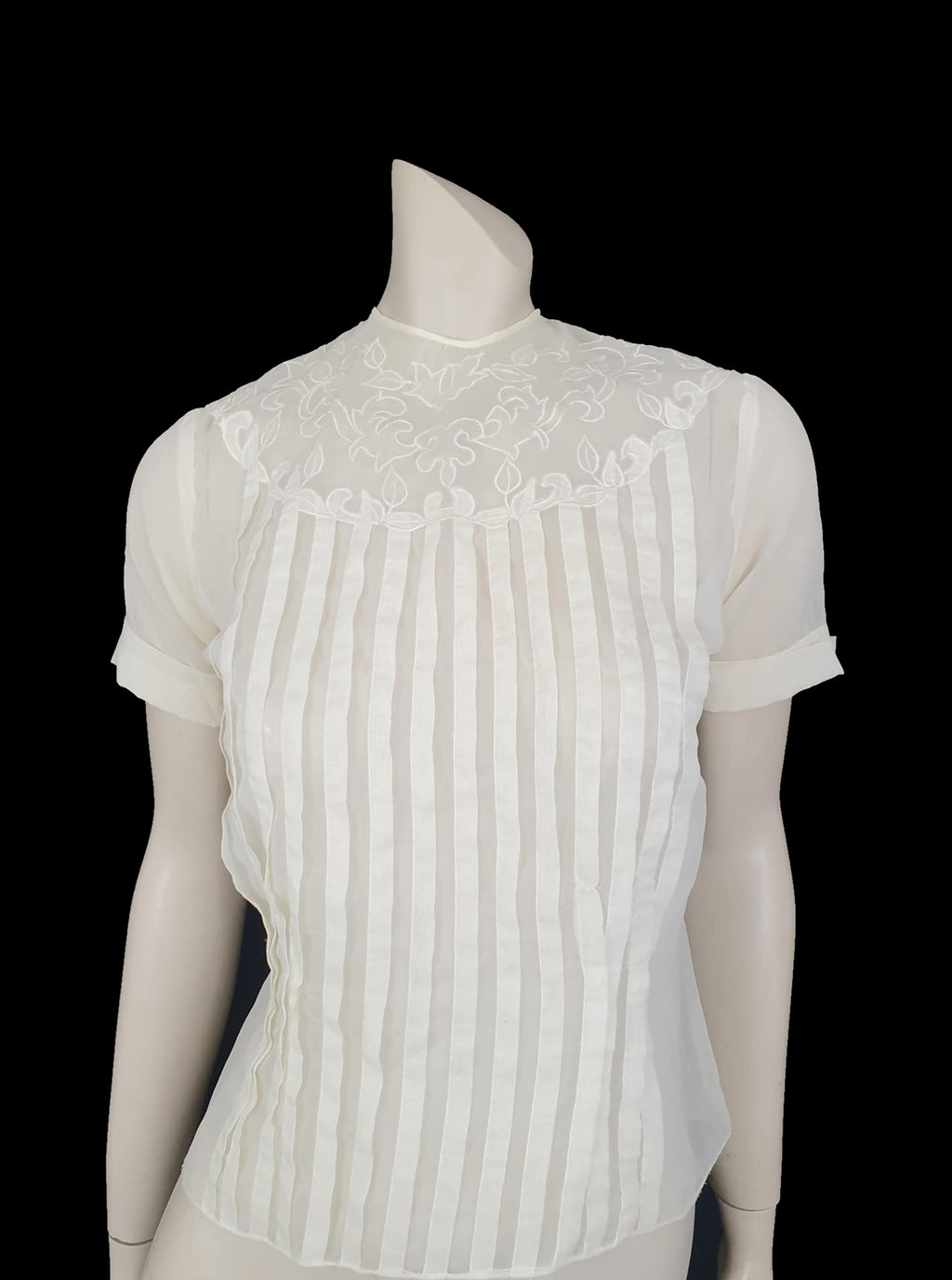 Beautiful little button back blouse - so pretty and feminine. Totally sheer nylon blouse has vertical tucks across the front and a circular yoke embellished with dainty applique work. The short sleeves have turn back cuffs. You will need to have someone to help you get dressed as it buttons down the back with shell buttons. It's darted in at the waist as it was designed to be tucked into a very high-waisted skirt. Brand is Park Lane, late 1950s-early 1960s. fits bust 92 cm/36".