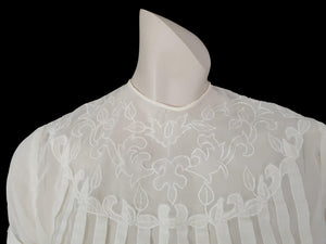 Beautiful little button back blouse - so pretty and feminine. Totally sheer nylon blouse has vertical tucks across the front and a circular yoke embellished with dainty applique work. The short sleeves have turn back cuffs. You will need to have someone to help you get dressed as it buttons down the back with shell buttons. It's darted in at the waist as it was designed to be tucked into a very high-waisted skirt. Brand is Park Lane, late 1950s-early 1960s. fits bust 92 cm/36".