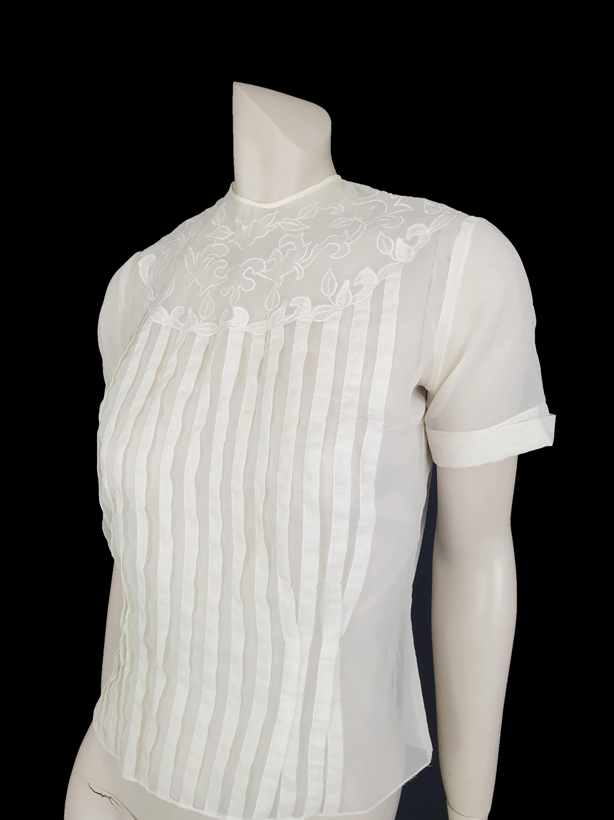 Beautiful little button back blouse - so pretty and feminine. Totally sheer nylon blouse has vertical tucks across the front and a circular yoke embellished with dainty applique work. The short sleeves have turn back cuffs. You will need to have someone to help you get dressed as it buttons down the back with shell buttons. It's darted in at the waist as it was designed to be tucked into a very high-waisted skirt. Brand is Park Lane, late 1950s-early 1960s. fits bust 92 cm/36".