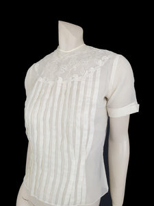 Beautiful little button back blouse - so pretty and feminine. Totally sheer nylon blouse has vertical tucks across the front and a circular yoke embellished with dainty applique work. The short sleeves have turn back cuffs. You will need to have someone to help you get dressed as it buttons down the back with shell buttons. It's darted in at the waist as it was designed to be tucked into a very high-waisted skirt. Brand is Park Lane, late 1950s-early 1960s. fits bust 92 cm/36".
