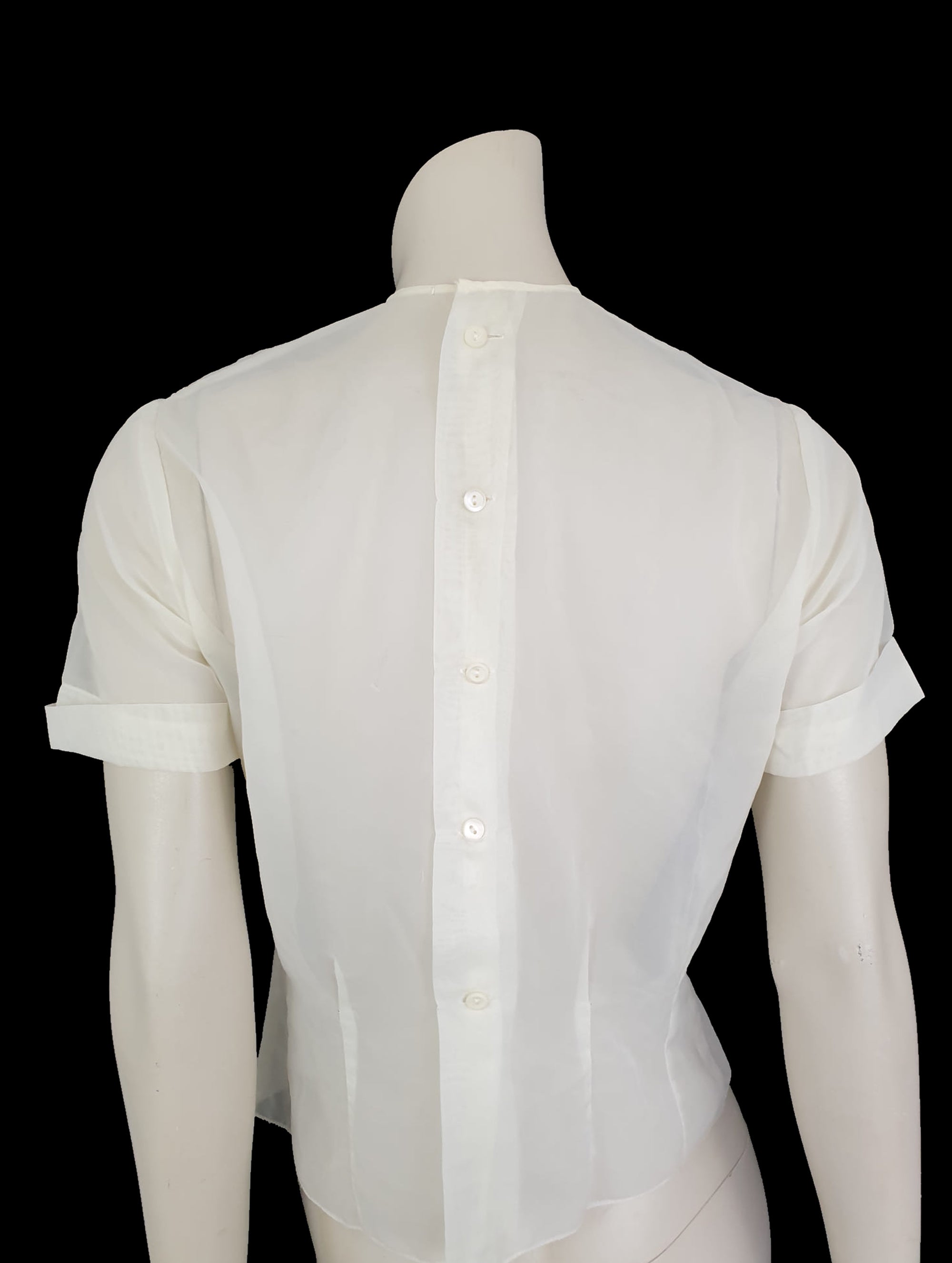 Beautiful little button back blouse - so pretty and feminine. Totally sheer nylon blouse has vertical tucks across the front and a circular yoke embellished with dainty applique work. The short sleeves have turn back cuffs. You will need to have someone to help you get dressed as it buttons down the back with shell buttons. It's darted in at the waist as it was designed to be tucked into a very high-waisted skirt. Brand is Park Lane, late 1950s-early 1960s. fits bust 92 cm/36".