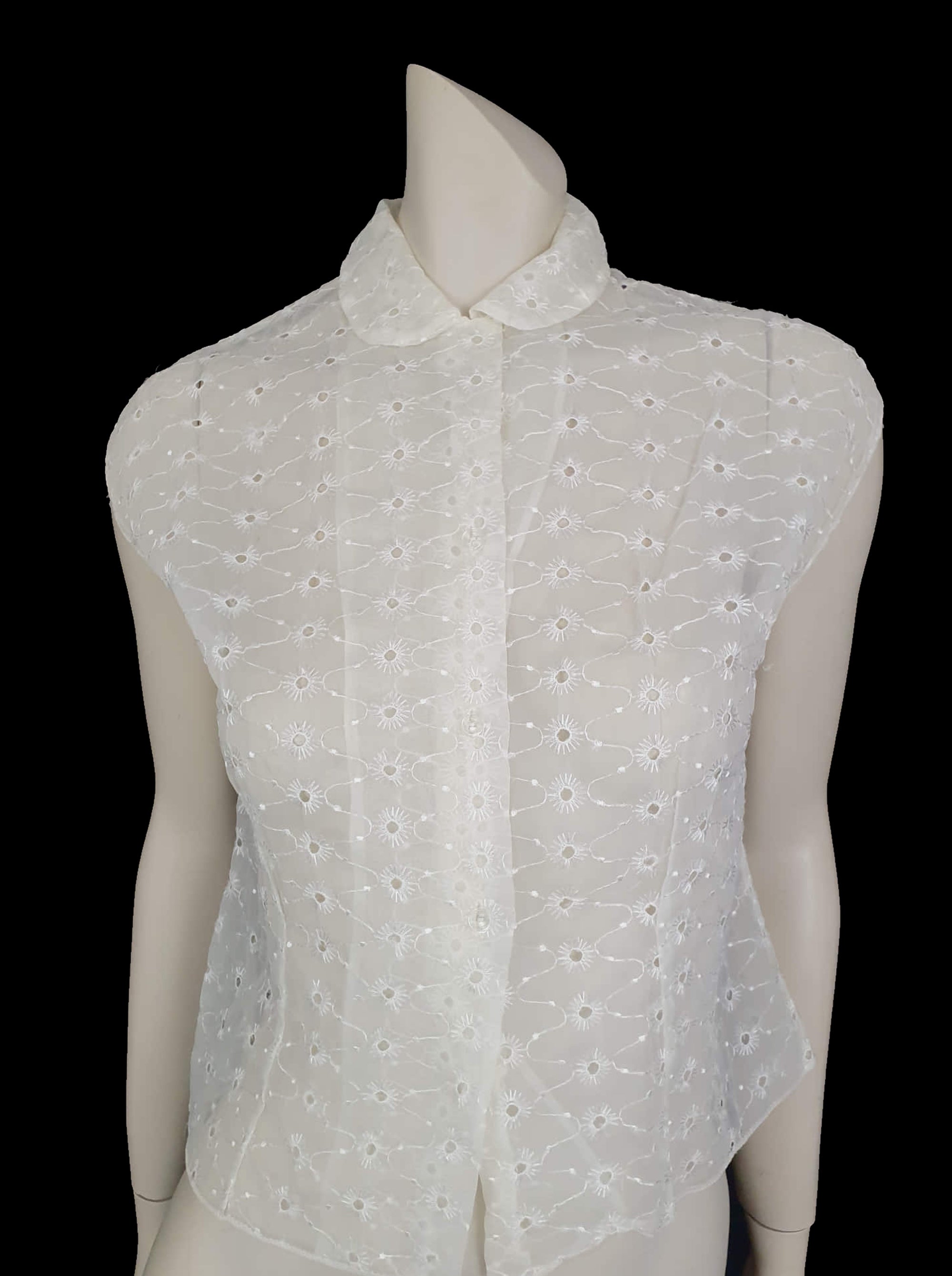 Beautiful sheer white nylon blouse embroidered all over in the eyelet style. 
The blouse has a peter pan collar and capped sleeves. It's darted in at the waist as it was designed to be worn with high waisted skirts. Closes to above waist level with clear plastic buttons. Fabric is nylon. No brand label. Late 1950s or very early 1960s. Medium