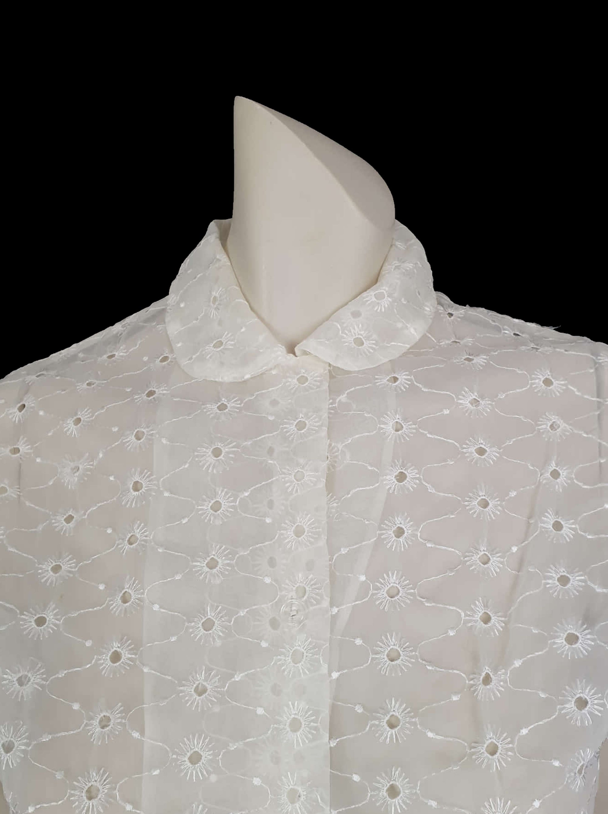 Beautiful sheer white nylon blouse embroidered all over in the eyelet style. 
The blouse has a peter pan collar and capped sleeves. It's darted in at the waist as it was designed to be worn with high waisted skirts. Closes to above waist level with clear plastic buttons. Fabric is nylon. No brand label. Late 1950s or very early 1960s. Medium