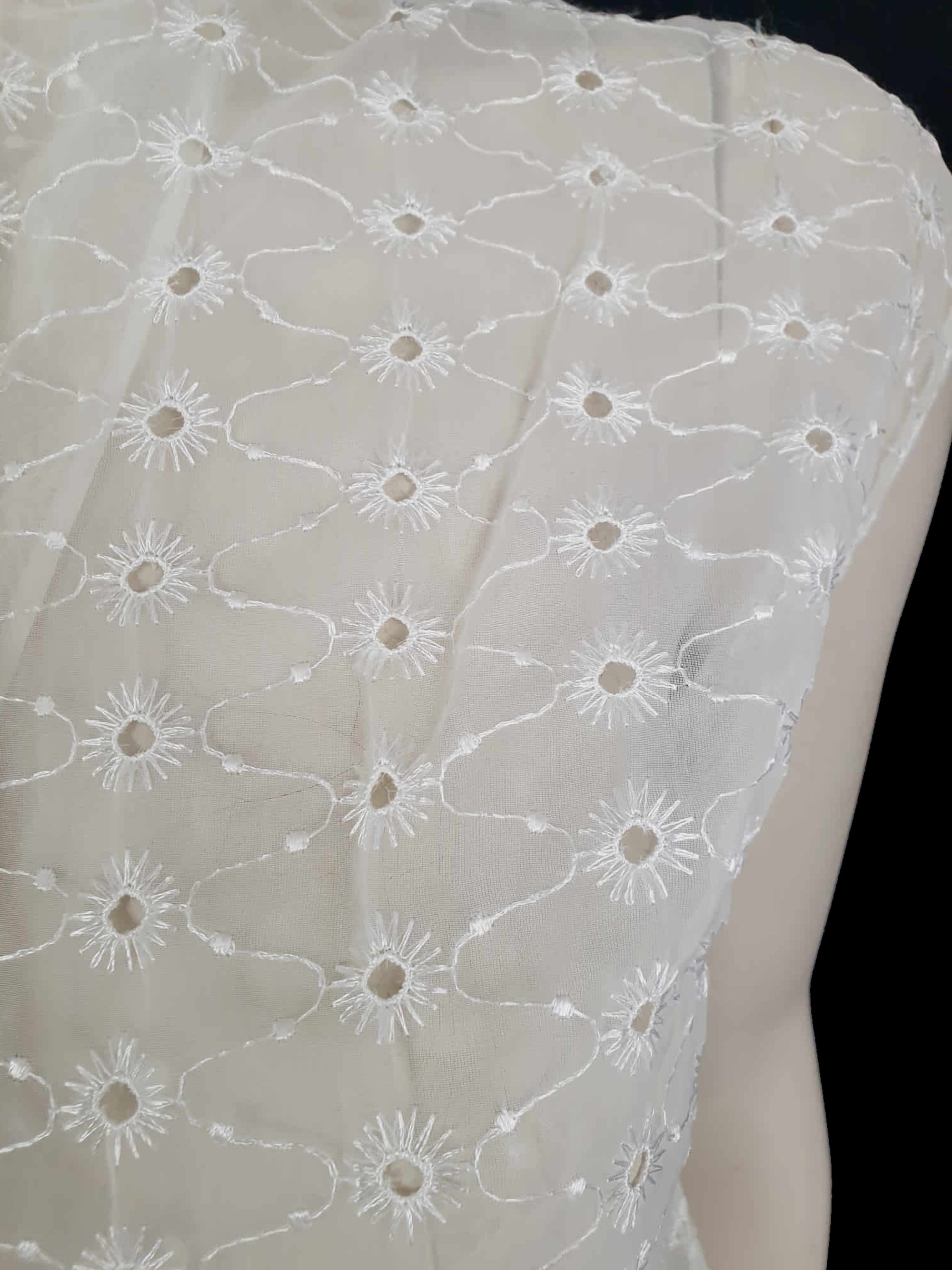 Beautiful sheer white nylon blouse embroidered all over in the eyelet style. 
The blouse has a peter pan collar and capped sleeves. It's darted in at the waist as it was designed to be worn with high waisted skirts. Closes to above waist level with clear plastic buttons. Fabric is nylon. No brand label. Late 1950s or very early 1960s. Medium