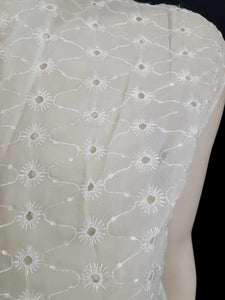 Beautiful sheer white nylon blouse embroidered all over in the eyelet style. 
The blouse has a peter pan collar and capped sleeves. It's darted in at the waist as it was designed to be worn with high waisted skirts. Closes to above waist level with clear plastic buttons. Fabric is nylon. No brand label. Late 1950s or very early 1960s. Medium