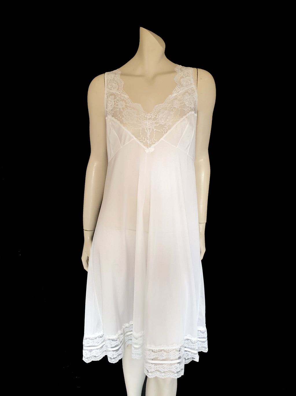 Below-knee to mid-calf length white midi slip has lace over the bust extending into wide front straps. Deep lace border also has ribbon trim. The straps are not adjustable. Fabric is nylon. Made in Australia. There is no brand label. 1980s-1990s. Medium