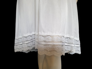 Below-knee to mid-calf length white midi slip has lace over the bust extending into wide front straps. Deep lace border also has ribbon trim. The straps are not adjustable. Fabric is nylon. Made in Australia. There is no brand label. 1980s-1990s. Medium