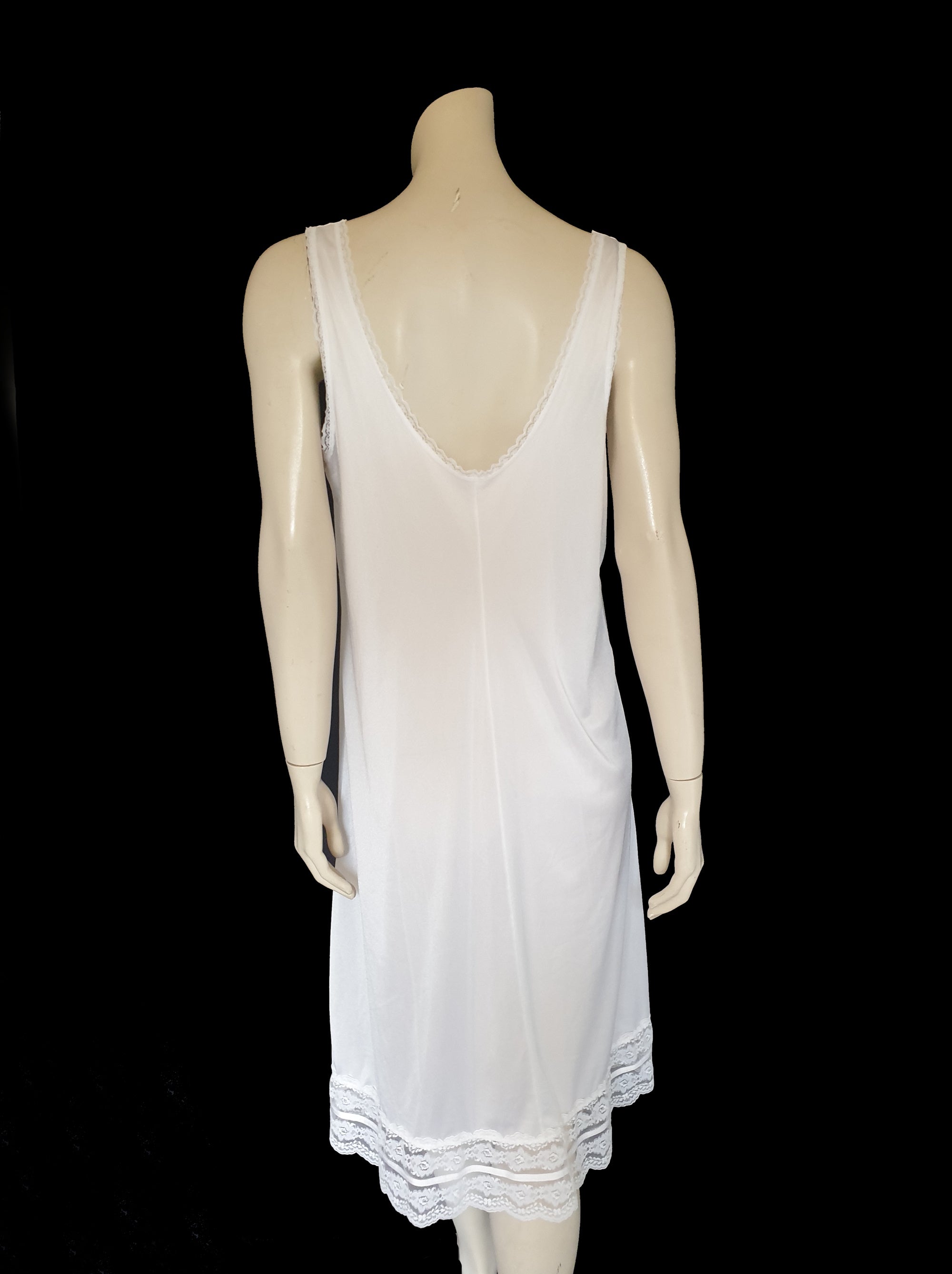 Below-knee to mid-calf length white midi slip has lace over the bust extending into wide front straps. Deep lace border also has ribbon trim. The straps are not adjustable. Fabric is nylon. Made in Australia. There is no brand label. 1980s-1990s. Medium
