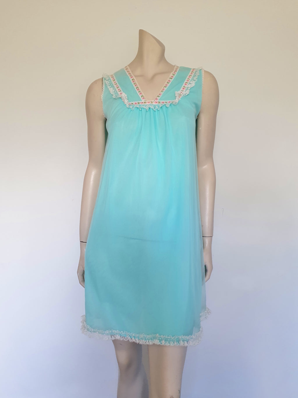 Very cute little aqua mini nightgown with floral braid and lace trim at the V neckline. The same lace also trims the hem. The nightie has a sheer overlay with an opaque layer of fabric beneath. Fabric is nylon. Brand is Irene Lingerie - Late 1960s - 1970s. Small.