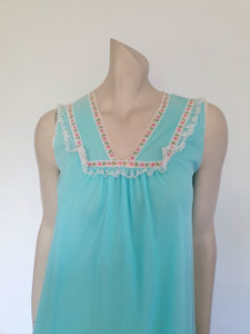 Very cute little aqua mini nightgown with floral braid and lace trim at the V neckline. The same lace also trims the hem. The nightie has a sheer overlay with an opaque layer of fabric beneath. Fabric is nylon. Brand is Irene Lingerie - Late 1960s - 1970s. Small.