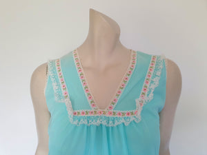 Very cute little aqua mini nightgown with floral braid and lace trim at the V neckline. The same lace also trims the hem. The nightie has a sheer overlay with an opaque layer of fabric beneath. Fabric is nylon. Brand is Irene Lingerie - Late 1960s - 1970s. Small.