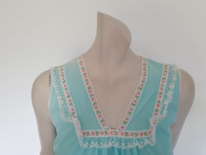 Very cute little aqua mini nightgown with floral braid and lace trim at the V neckline. The same lace also trims the hem. The nightie has a sheer overlay with an opaque layer of fabric beneath. Fabric is nylon. Brand is Irene Lingerie - Late 1960s - 1970s. Small.