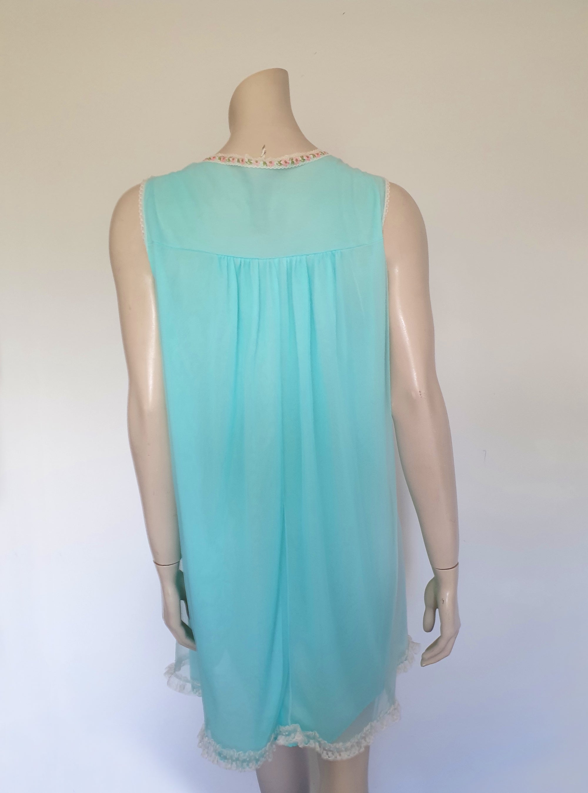 Very cute little aqua mini nightgown with floral braid and lace trim at the V neckline. The same lace also trims the hem. The nightie has a sheer overlay with an opaque layer of fabric beneath. Fabric is nylon. Brand is Irene Lingerie - Late 1960s - 1970s. Small.