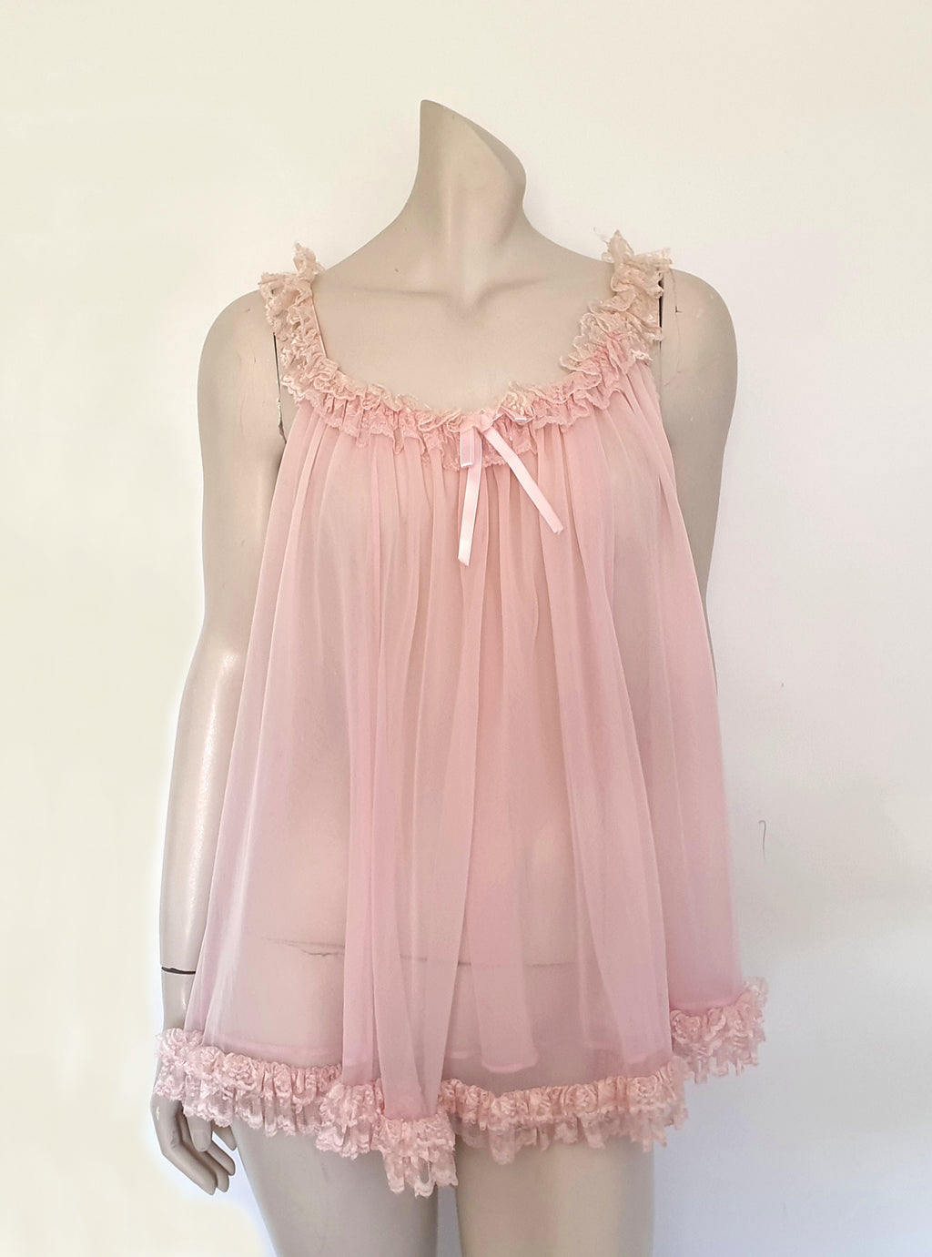 Pink Babydoll has a wide scooped neckline extending into straps. The neckline and the straps are  on elastic and are trimmed with wide ruffled lace. The same lace trims the hem. Ribbon bow at the front. The underarms are also elasticised. It's made from two layers of sheer nylon. Label reads S.G. for Escante, and appears to be a reproduction of the popular '60 style made likely in the 1990s. Extra large, marked 3XL