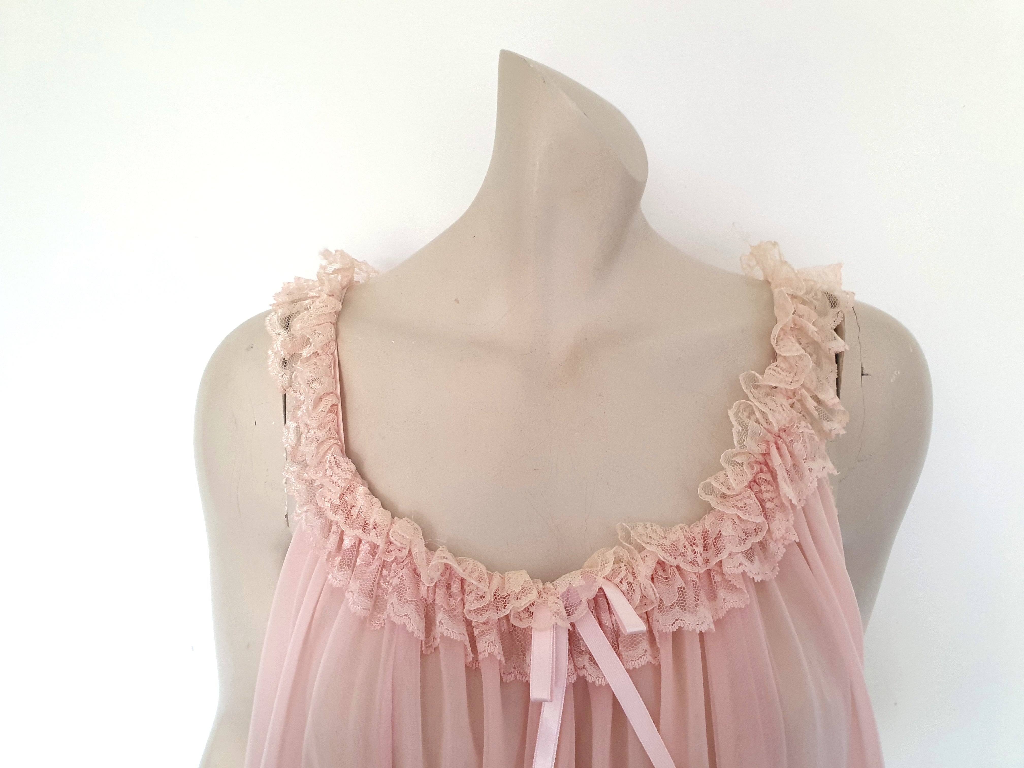 Pink Babydoll has a wide scooped neckline extending into straps. The neckline and the straps are  on elastic and are trimmed with wide ruffled lace. The same lace trims the hem. Ribbon bow at the front. The underarms are also elasticised. It's made from two layers of sheer nylon. Label reads S.G. for Escante, and appears to be a reproduction of the popular '60 style made likely in the 1990s. Extra large, marked 3XL