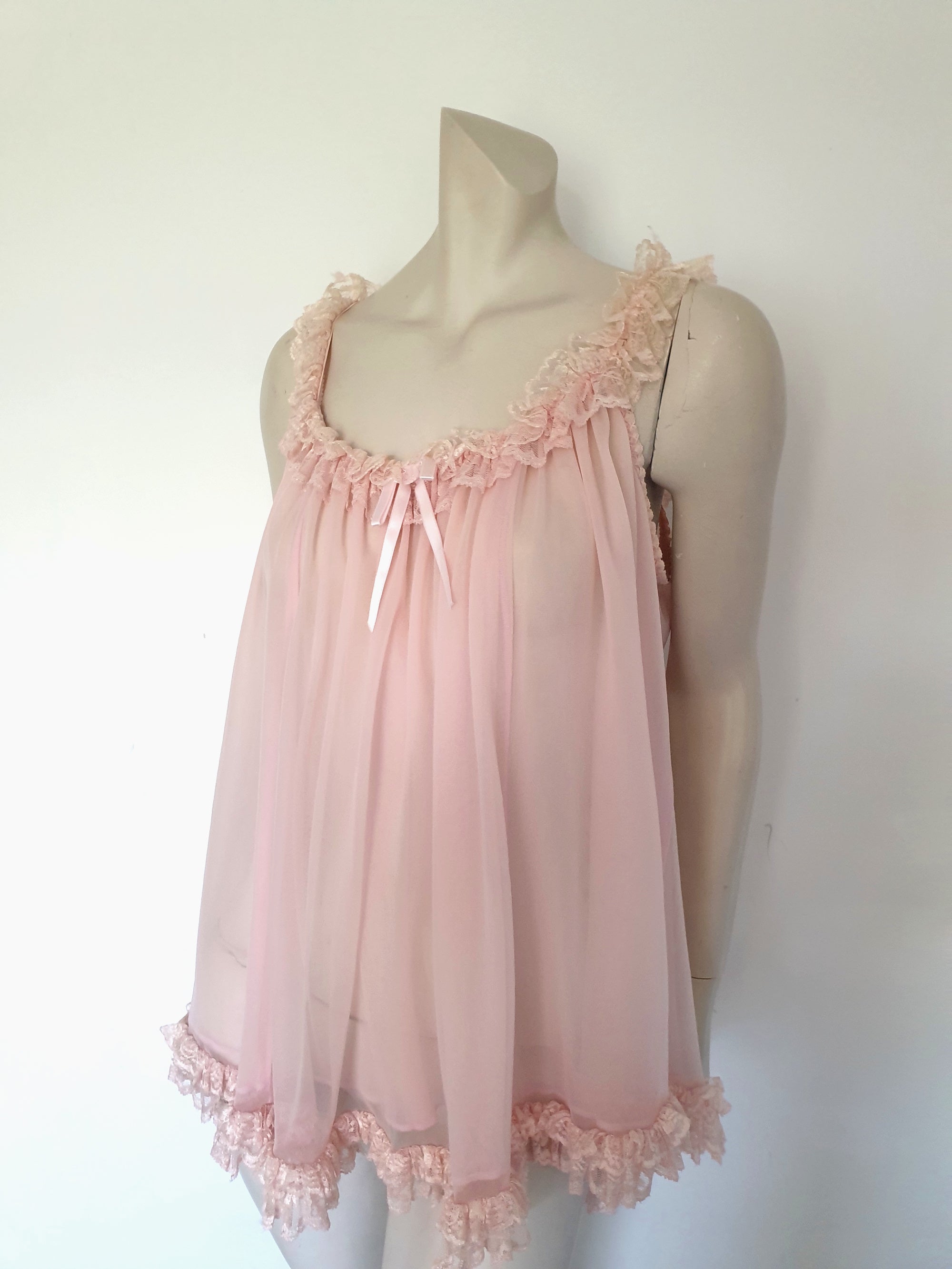 Pink Babydoll has a wide scooped neckline extending into straps. The neckline and the straps are  on elastic and are trimmed with wide ruffled lace. The same lace trims the hem. Ribbon bow at the front. The underarms are also elasticised. It's made from two layers of sheer nylon. Label reads S.G. for Escante, and appears to be a reproduction of the popular '60 style made likely in the 1990s. Extra large, marked 3XL